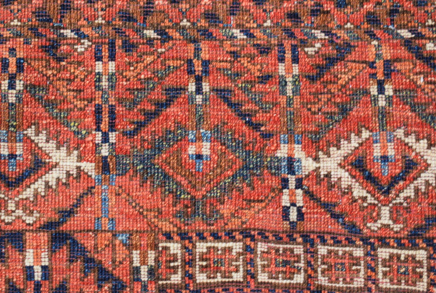 A close-up of a handwoven Afghan Chobi rug featuring geometric patterns in warm red and blue tones.