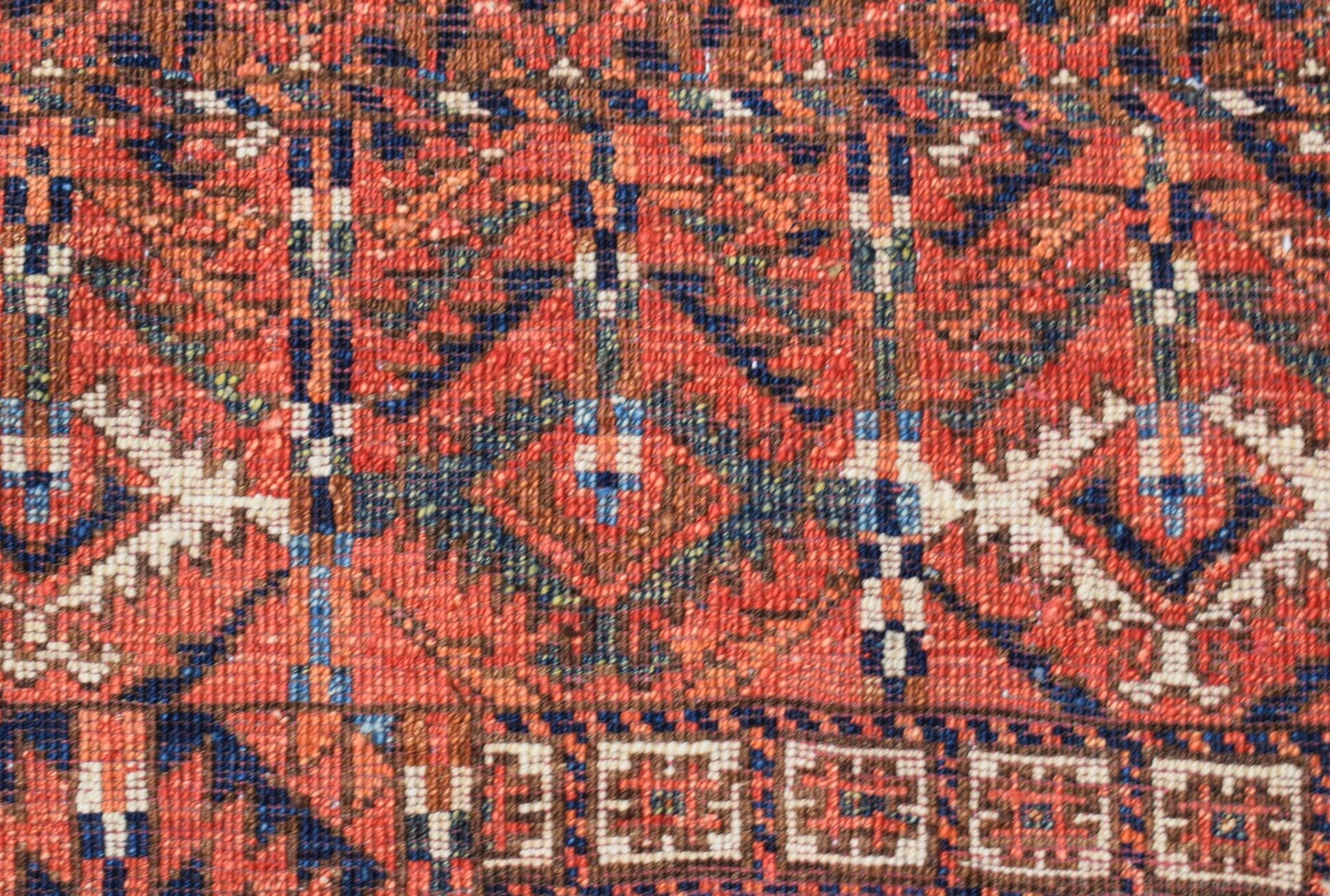 A close-up of a handwoven Afghan Chobi rug featuring geometric patterns in warm red and blue tones.