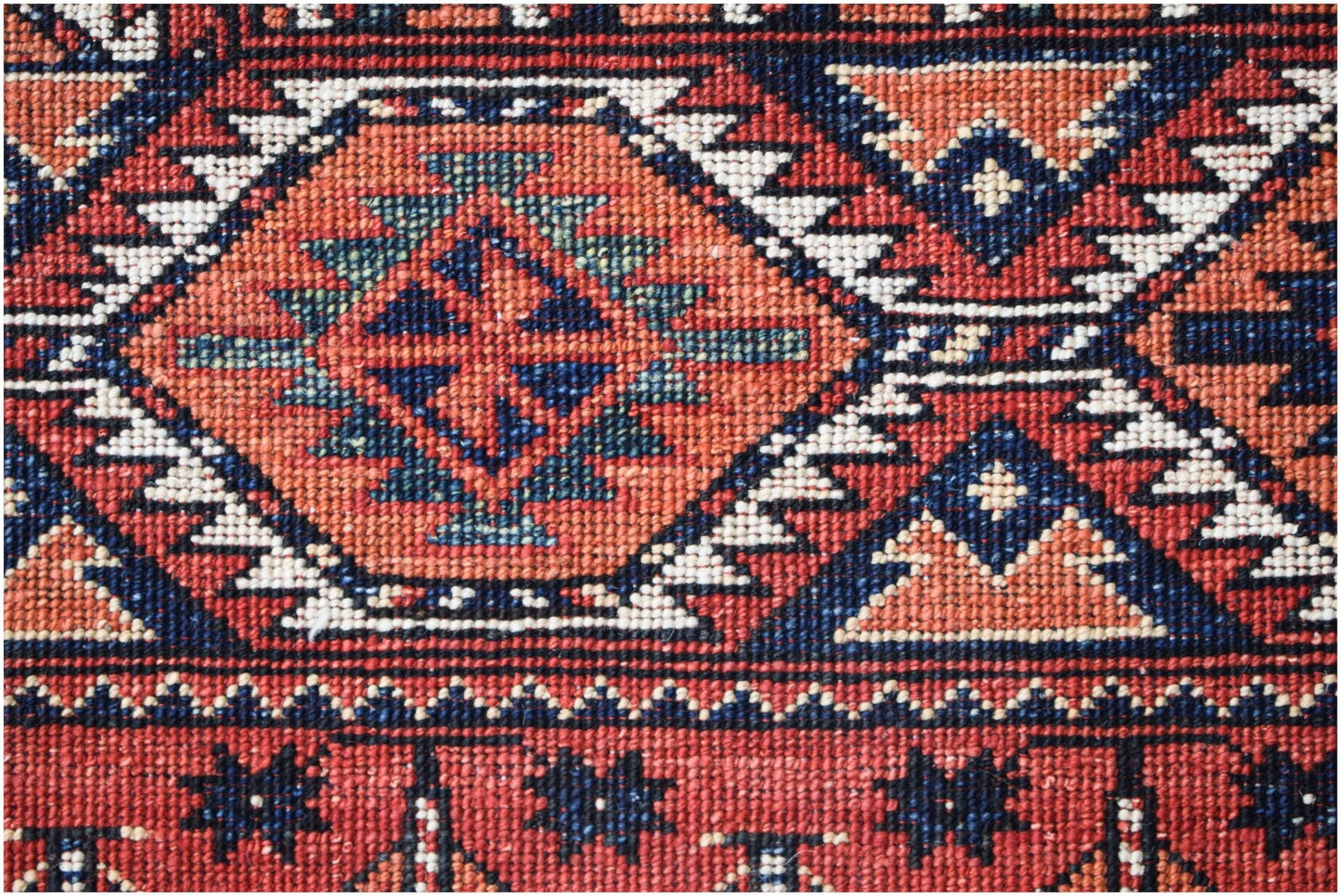 A close-up of an Afghan Chobi rug featuring a geometric diamond pattern in red, blue, and cream.
