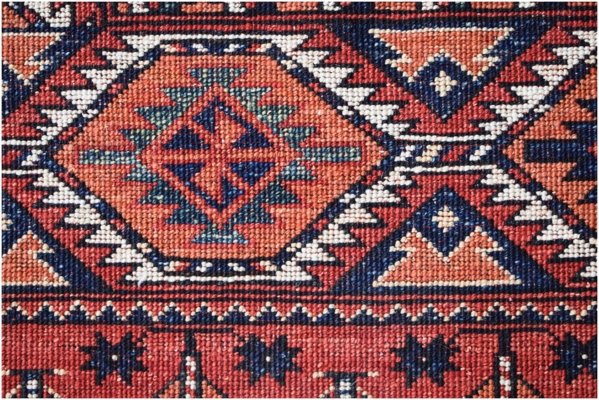 A close-up of an Afghan Chobi rug featuring a geometric diamond pattern in red, blue, and cream.