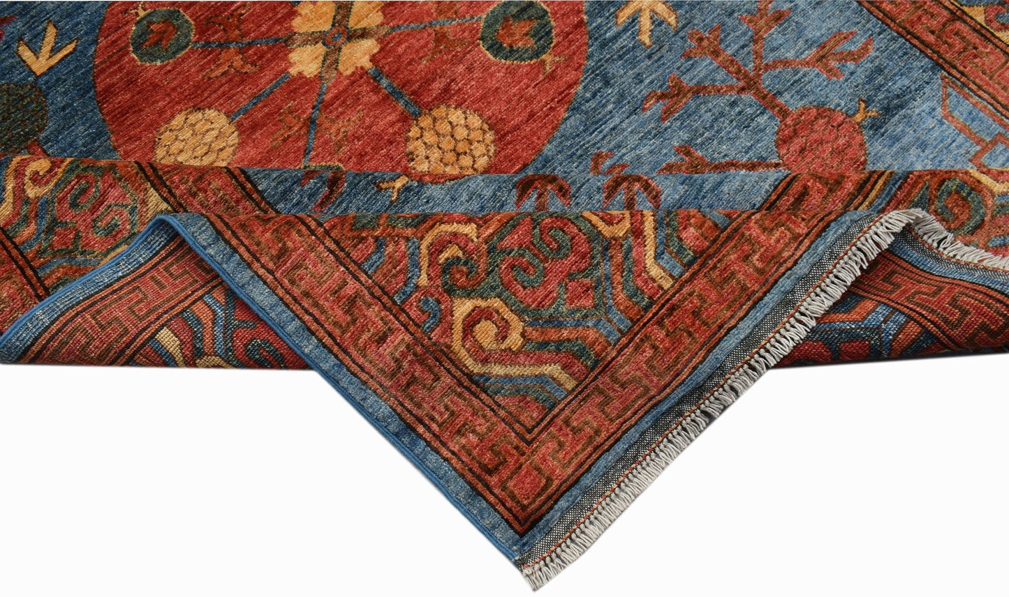 A handwoven Afghan Chobi rug featuring a red circular medallion on a blue field with fringe.