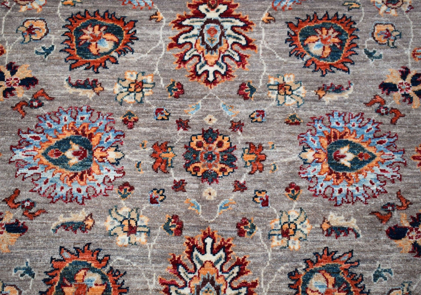 A handwoven Afghan Chobi rug featuring a traditional floral pattern in orange, blue, and cream.