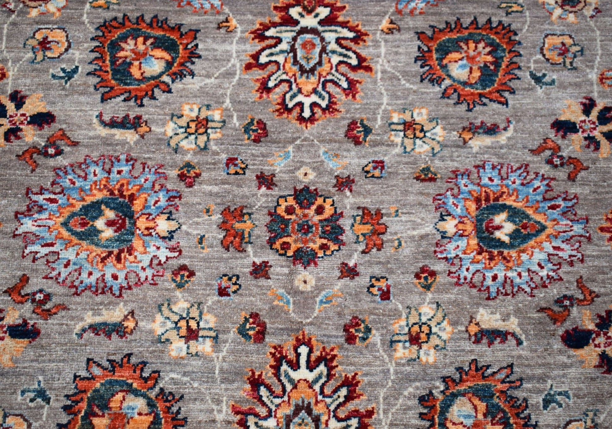 A handwoven Afghan Chobi rug featuring a traditional floral pattern in orange, blue, and cream.