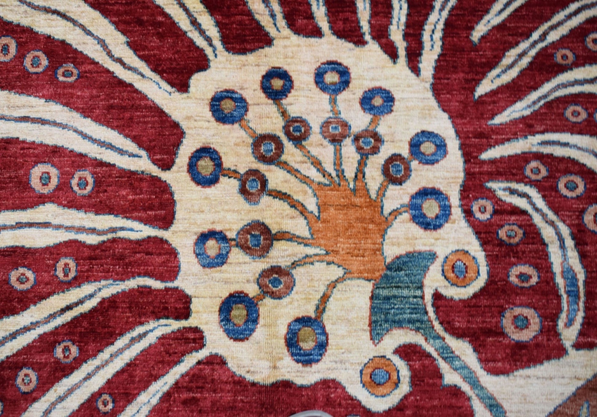 A close-up of an Afghan Chobi rug featuring a stylized floral motif in red, cream, and blue tones.