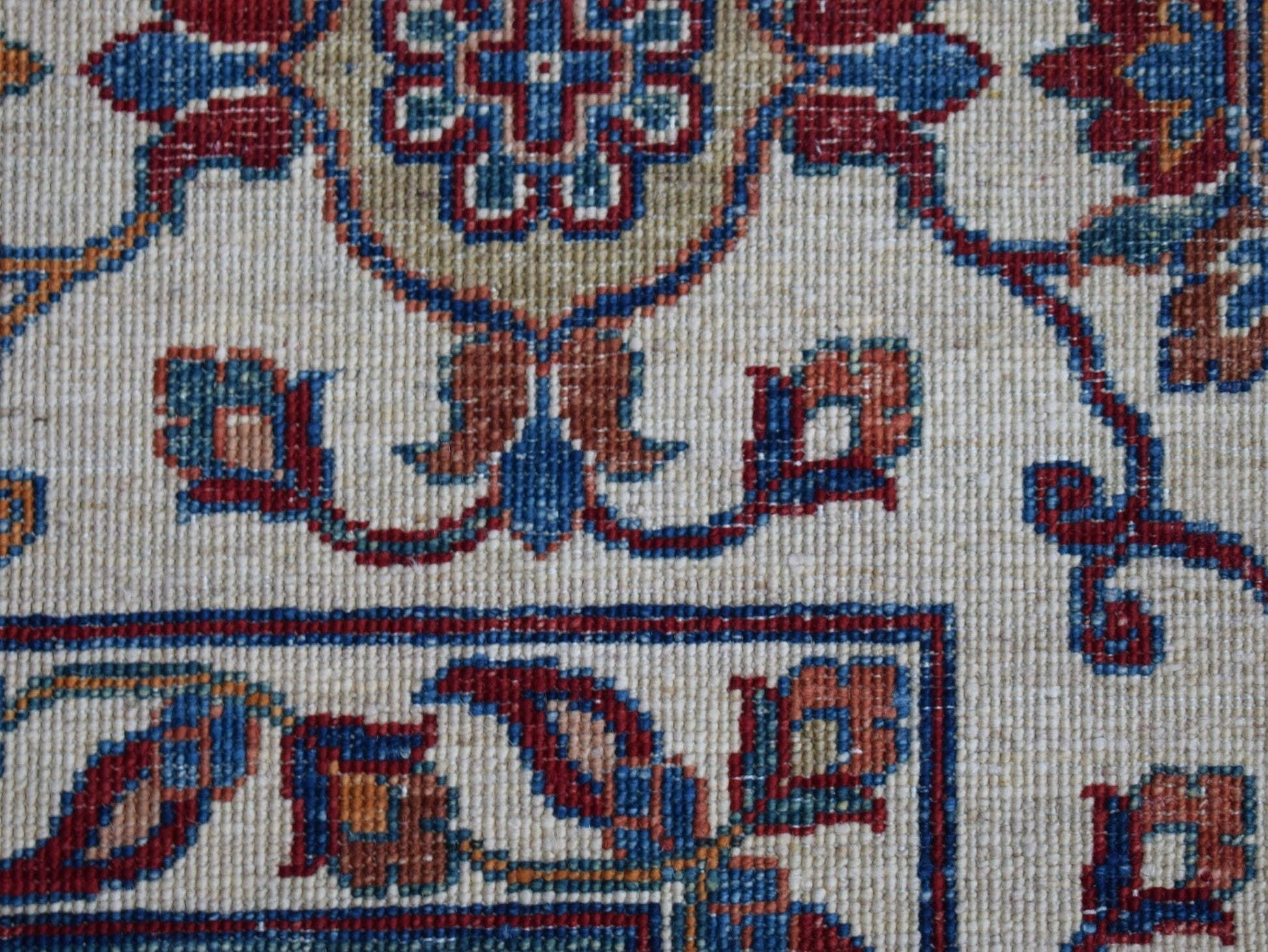 A close-up of an Afghan Chobi rug featuring intricate floral patterns in red, blue, and tan wool.