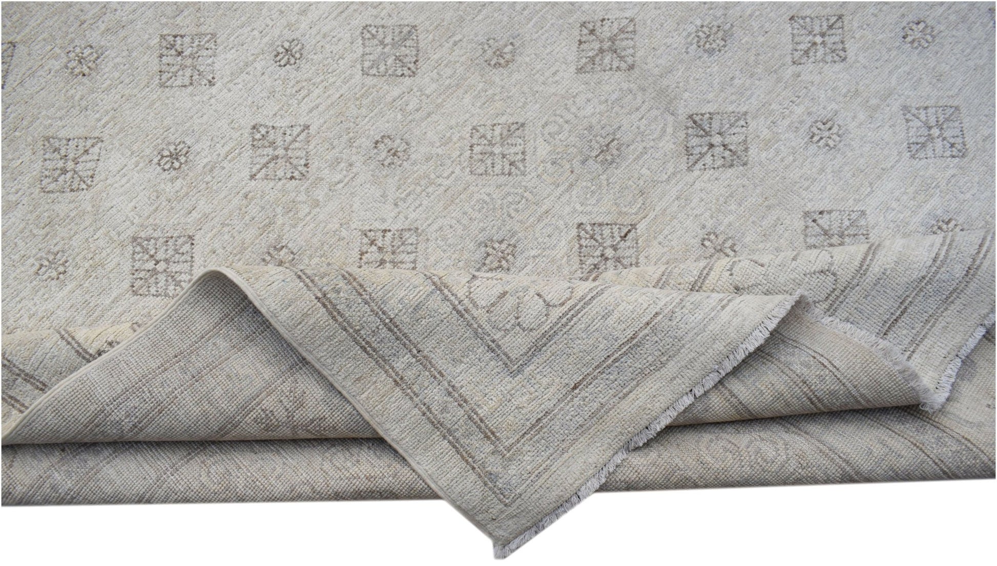 A handmade Afghan Chobi rug featuring a light beige field with geometric patterns and a folded corner.