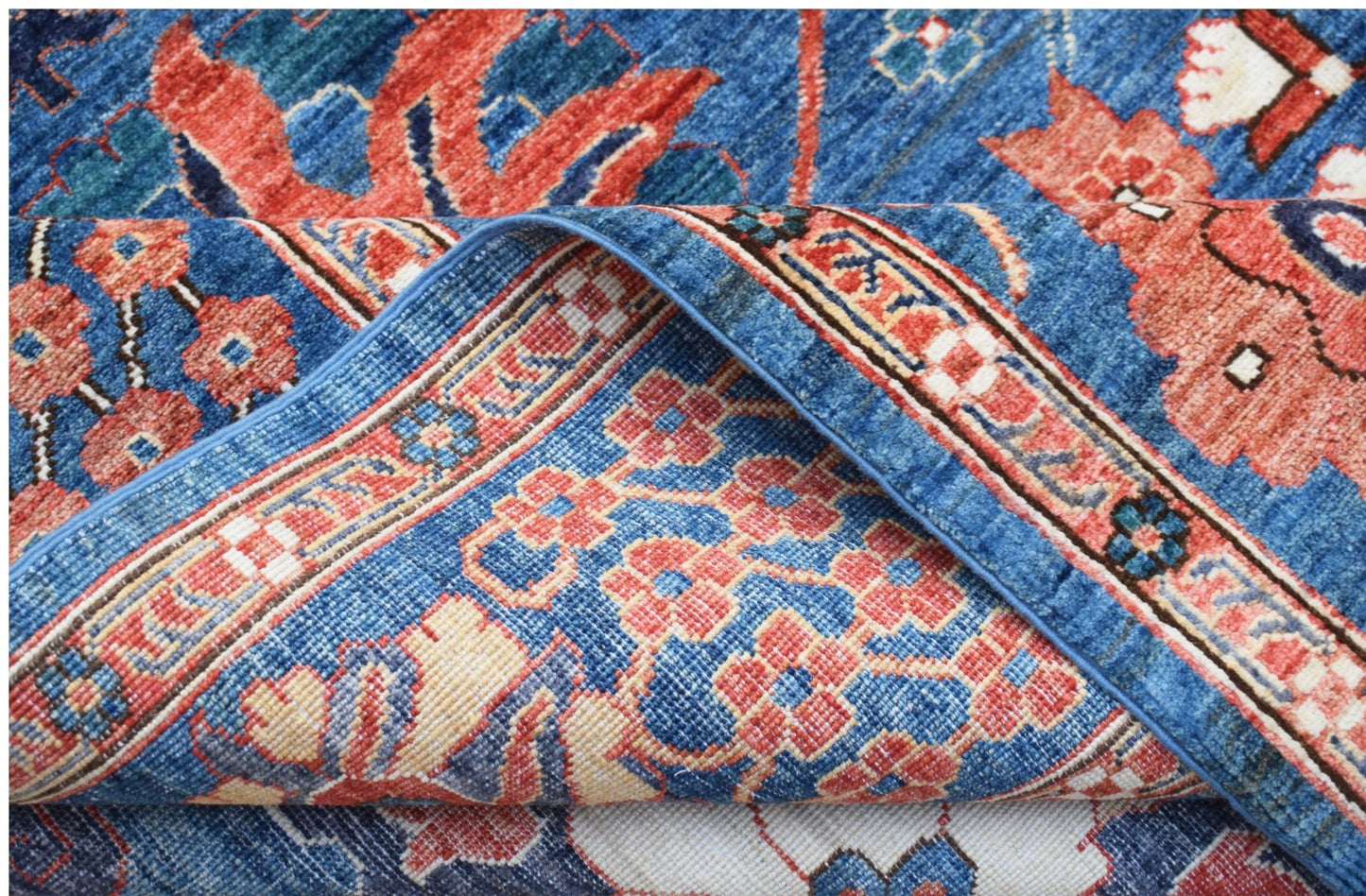 A close-up of a handwoven Afghan Chobi rug featuring traditional floral patterns in blue and red.