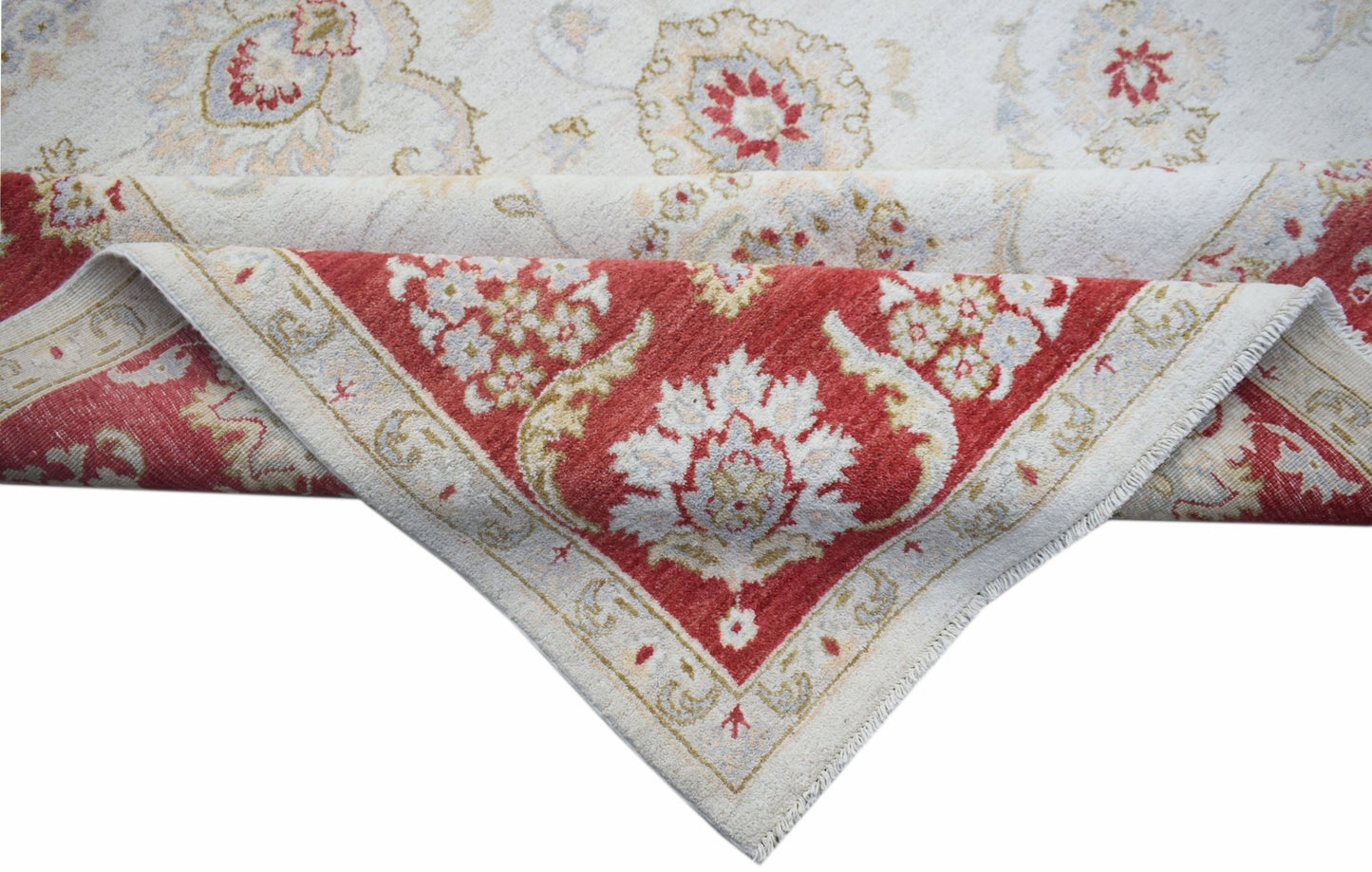 A handwoven Afghan Chobi rug with a cream field and a red floral border folded at the corner.