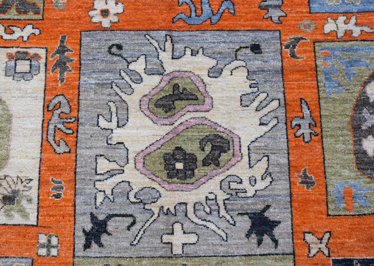 A handwoven Afghan Chobi rug featuring a central abstract motif on a grey field with orange borders.
