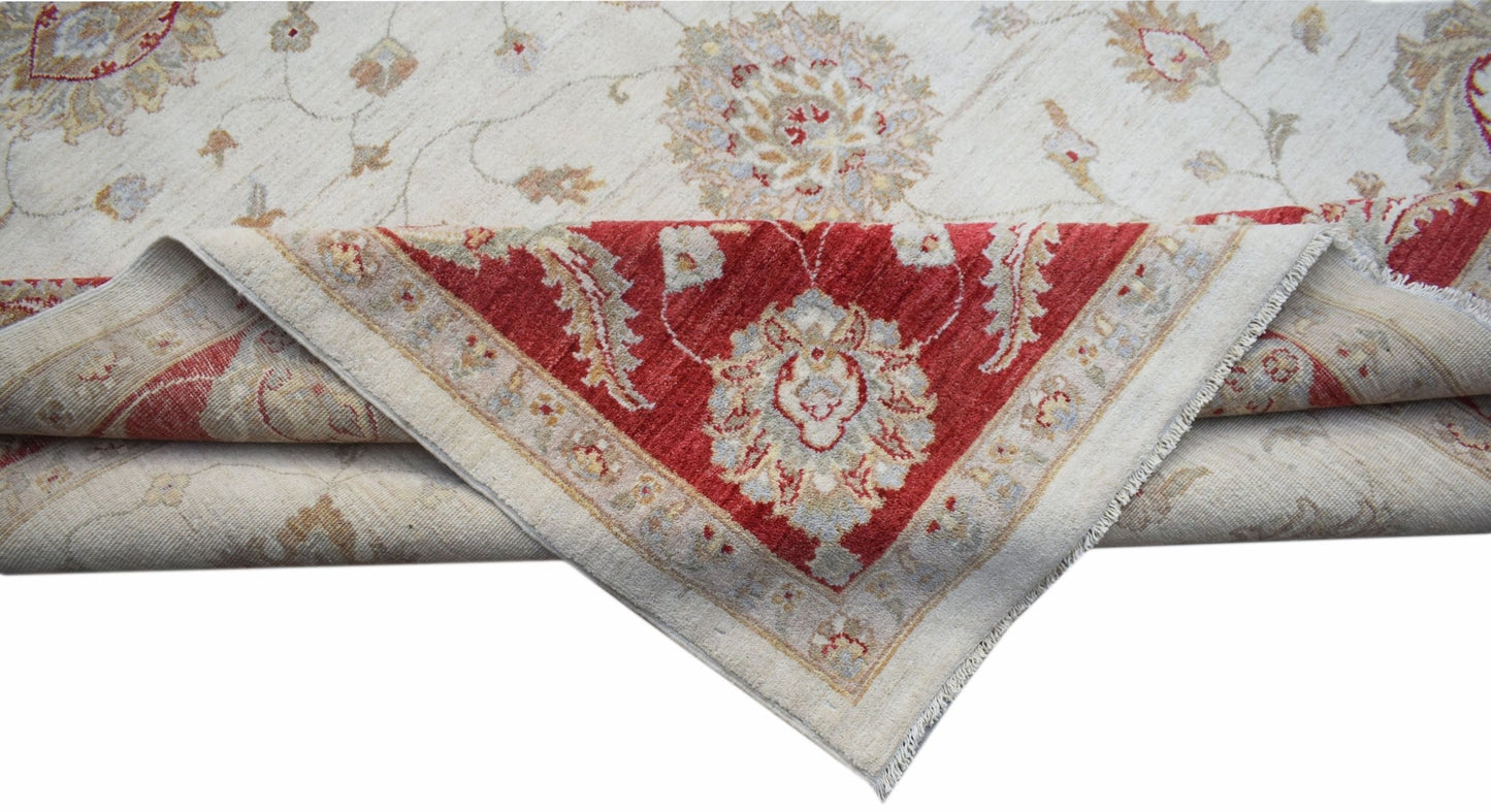 A handwoven Afghan Chobi rug with a cream field and a folded corner revealing a red border.