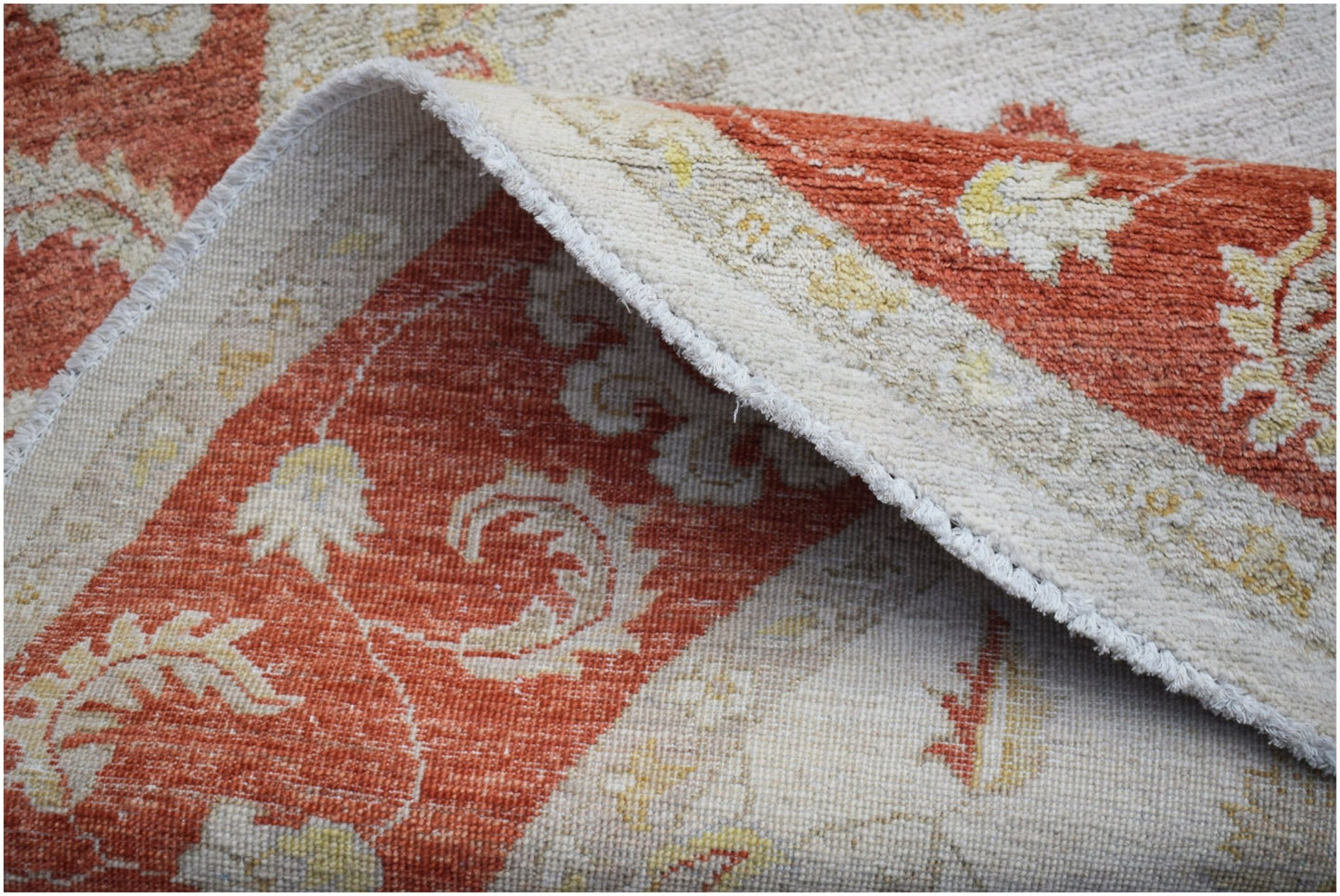 A corner of a square Afghan Chobi rug with a traditional floral pattern in rust and cream tones.