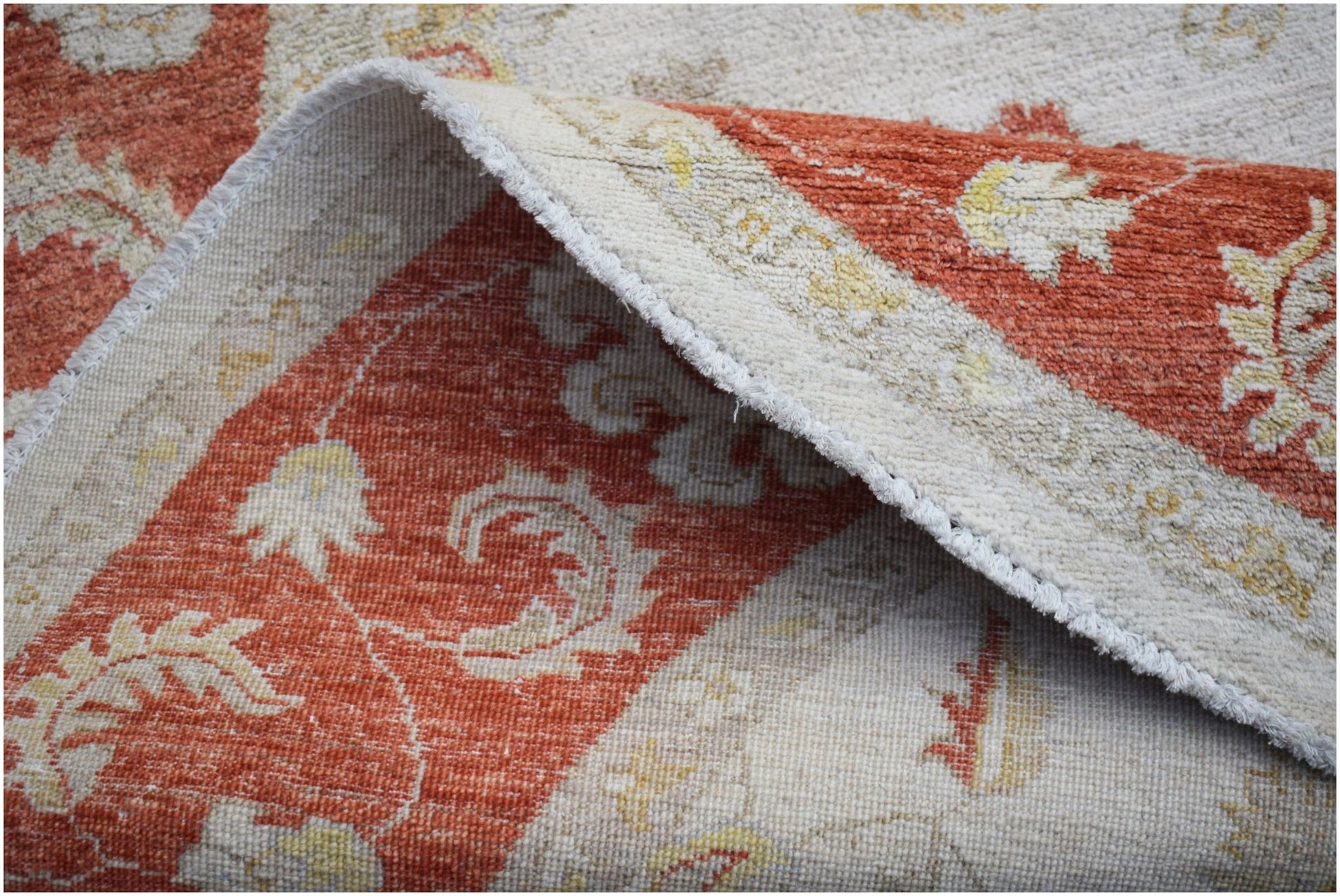 A corner of a square Afghan Chobi rug with a traditional floral pattern in rust and cream tones.