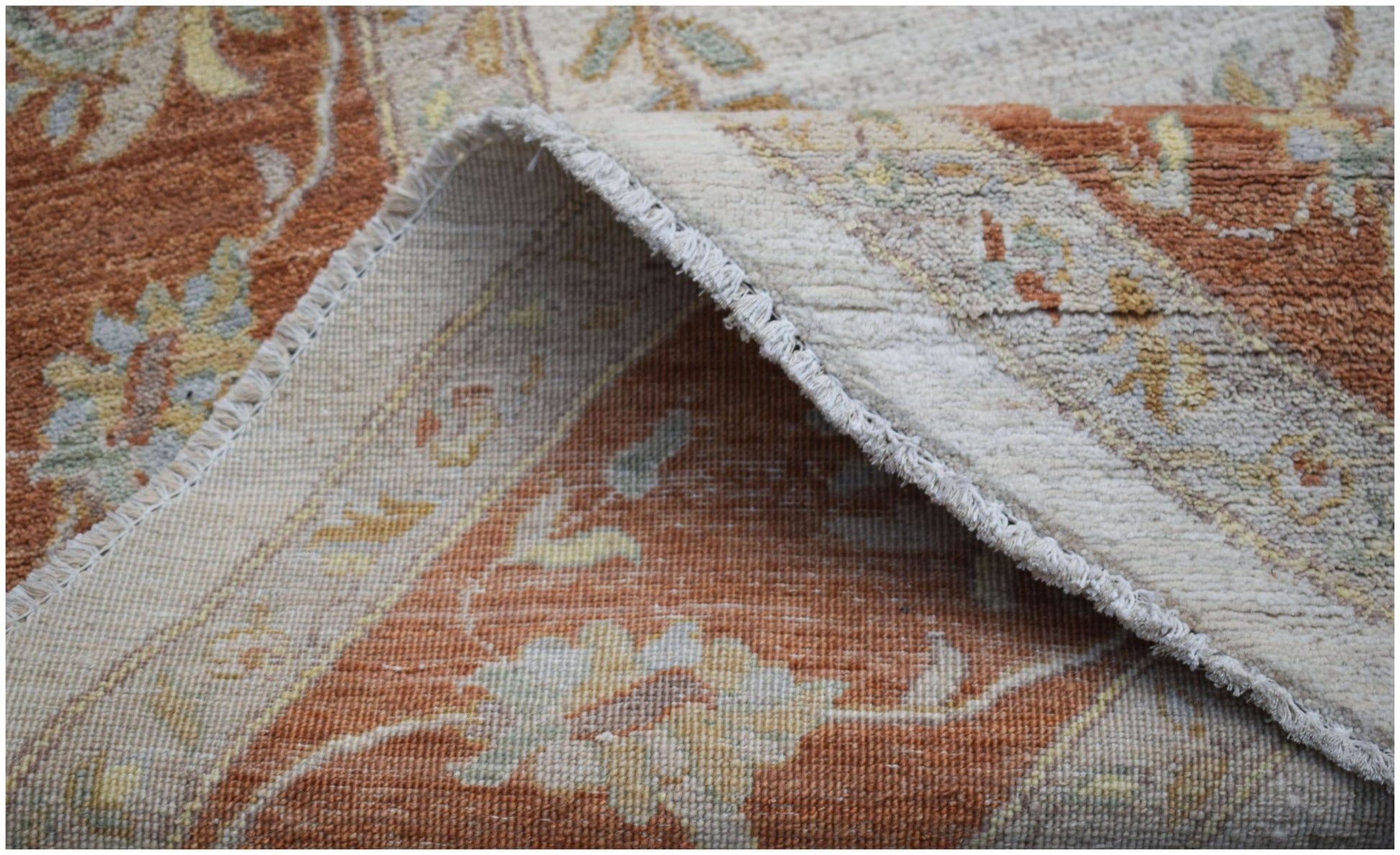 A folded Afghan Chobi rug featuring traditional floral patterns in earthy orange and cream tones.