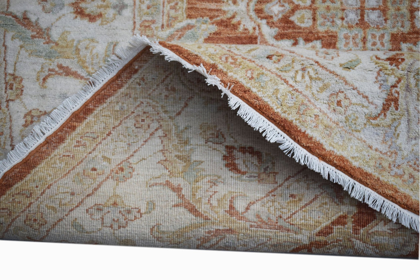 A folded Afghan Chobi rug featuring a traditional floral pattern in earthy orange and cream tones.