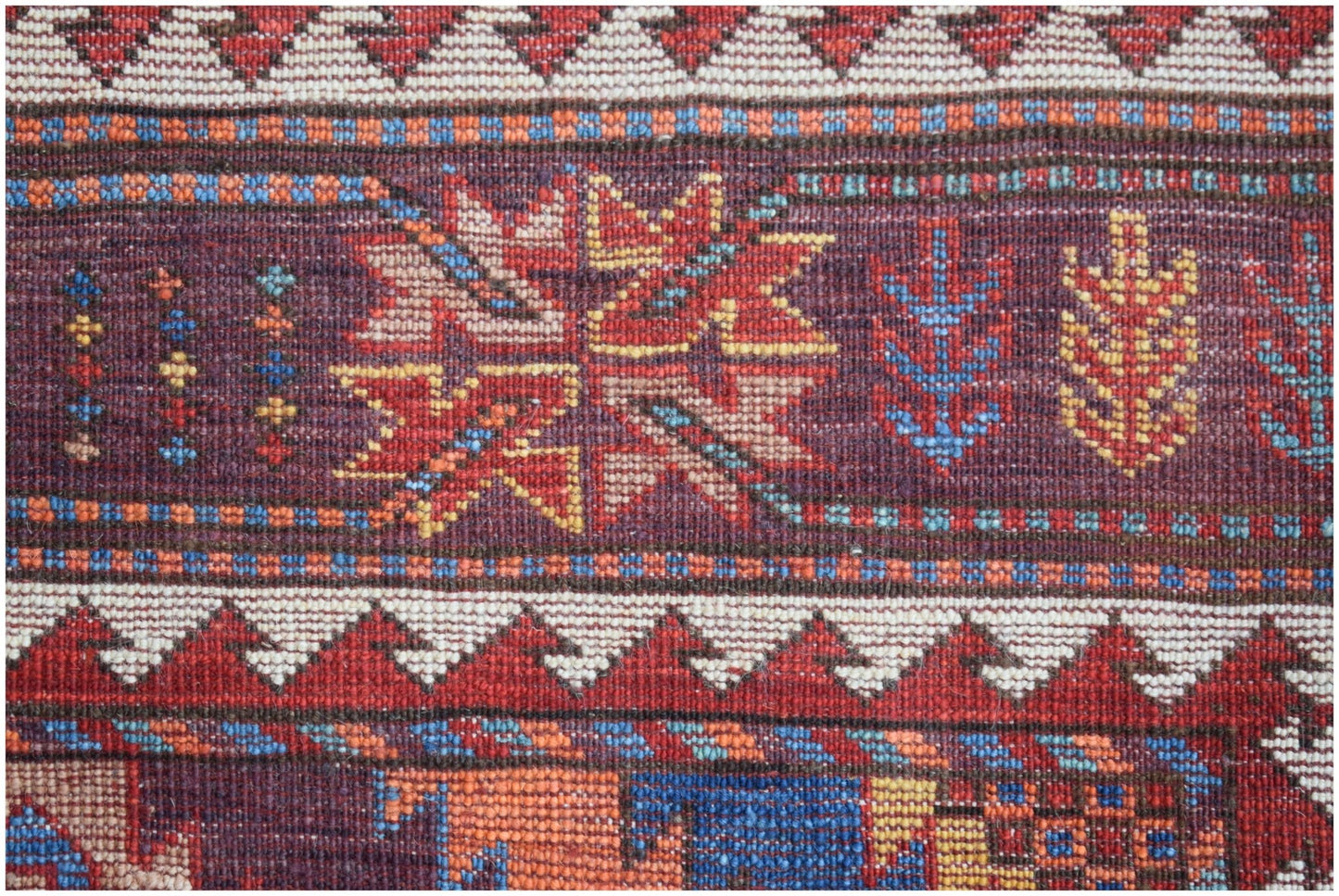 A close-up of a handwoven Afghan rug featuring geometric floral motifs in red, blue, and yellow.