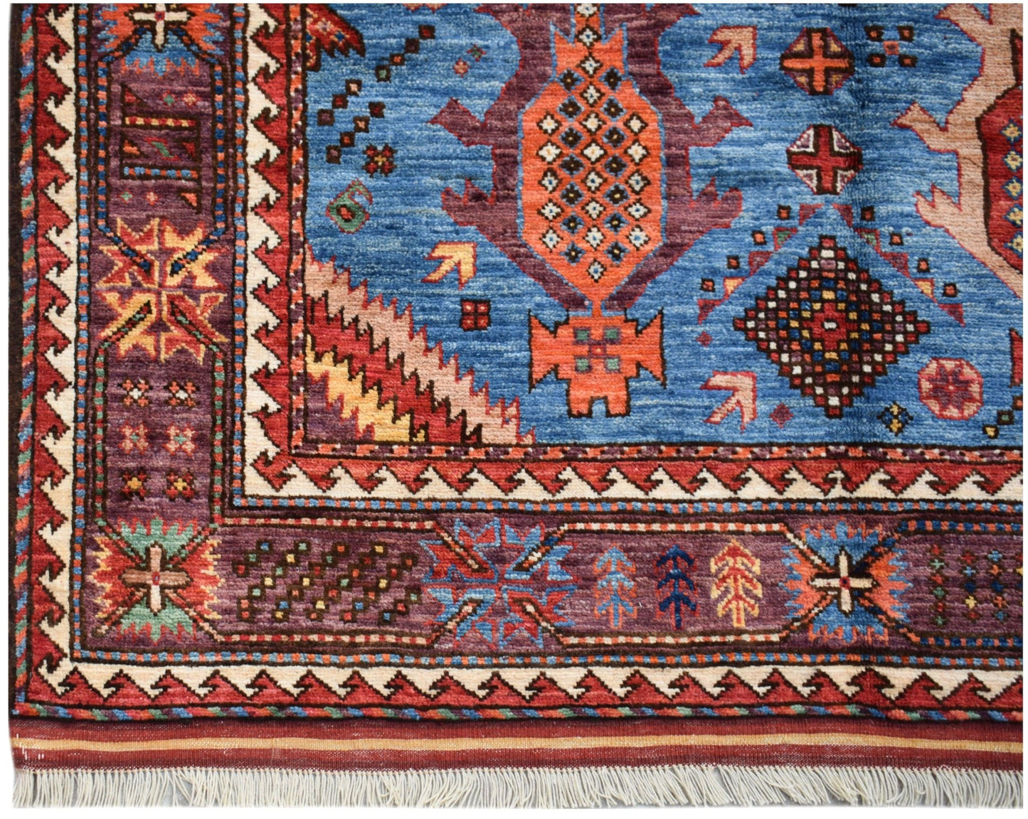 Handwoven Afghan Herati rug featuring a blue field with geometric patterns and a purple border.