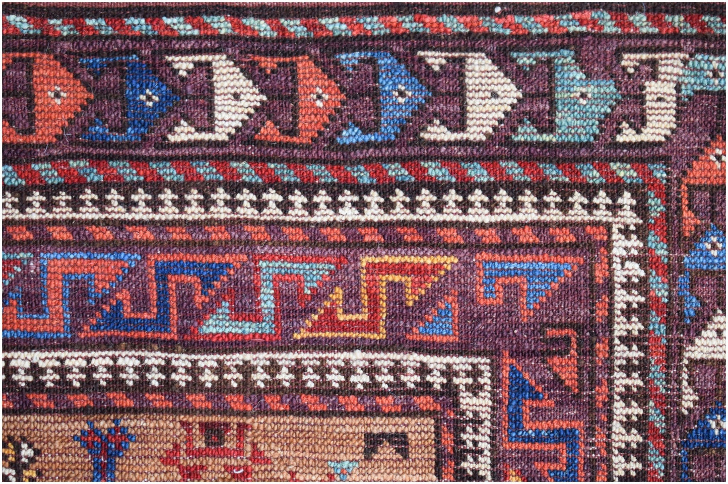 A close-up of an Afghan Herati rug featuring intricate geometric patterns in red, blue, and cream.