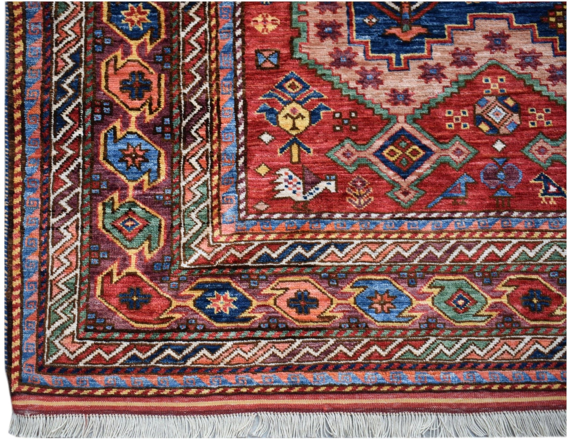 A handmade Afghan Herati rug featuring a red field with geometric patterns and a fringed edge.