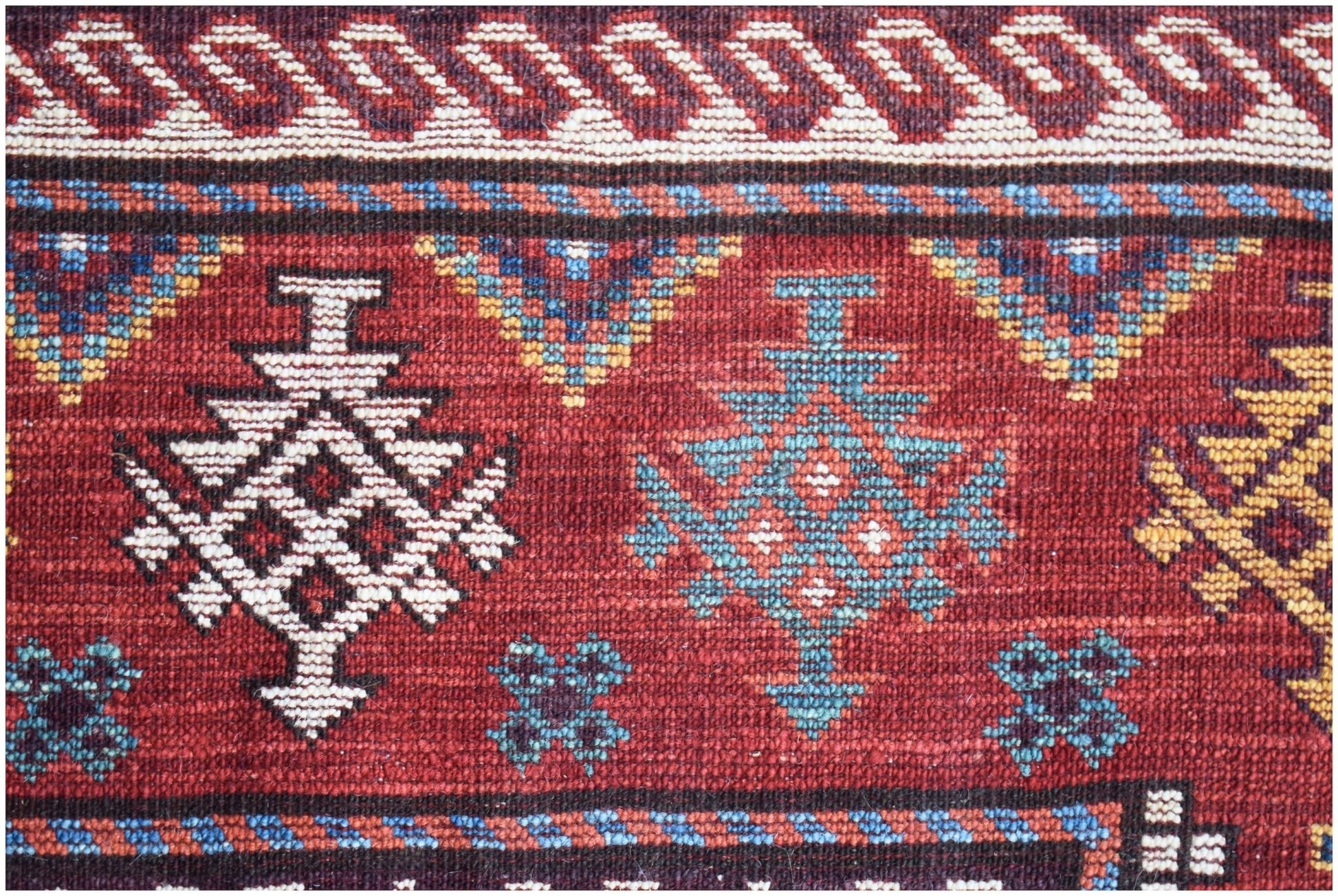 A close-up of a handwoven Afghan Herati rug featuring geometric patterns in red, blue, and cream.