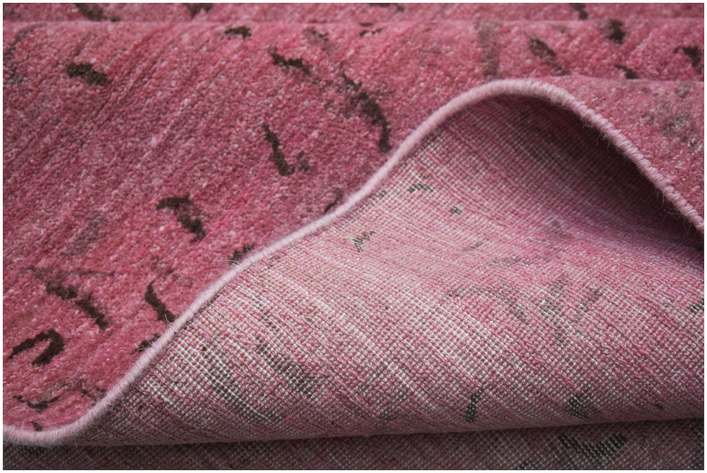 A close-up of a pink overdyed Afghan Chobi rug showing its handwoven wool texture and cotton base.