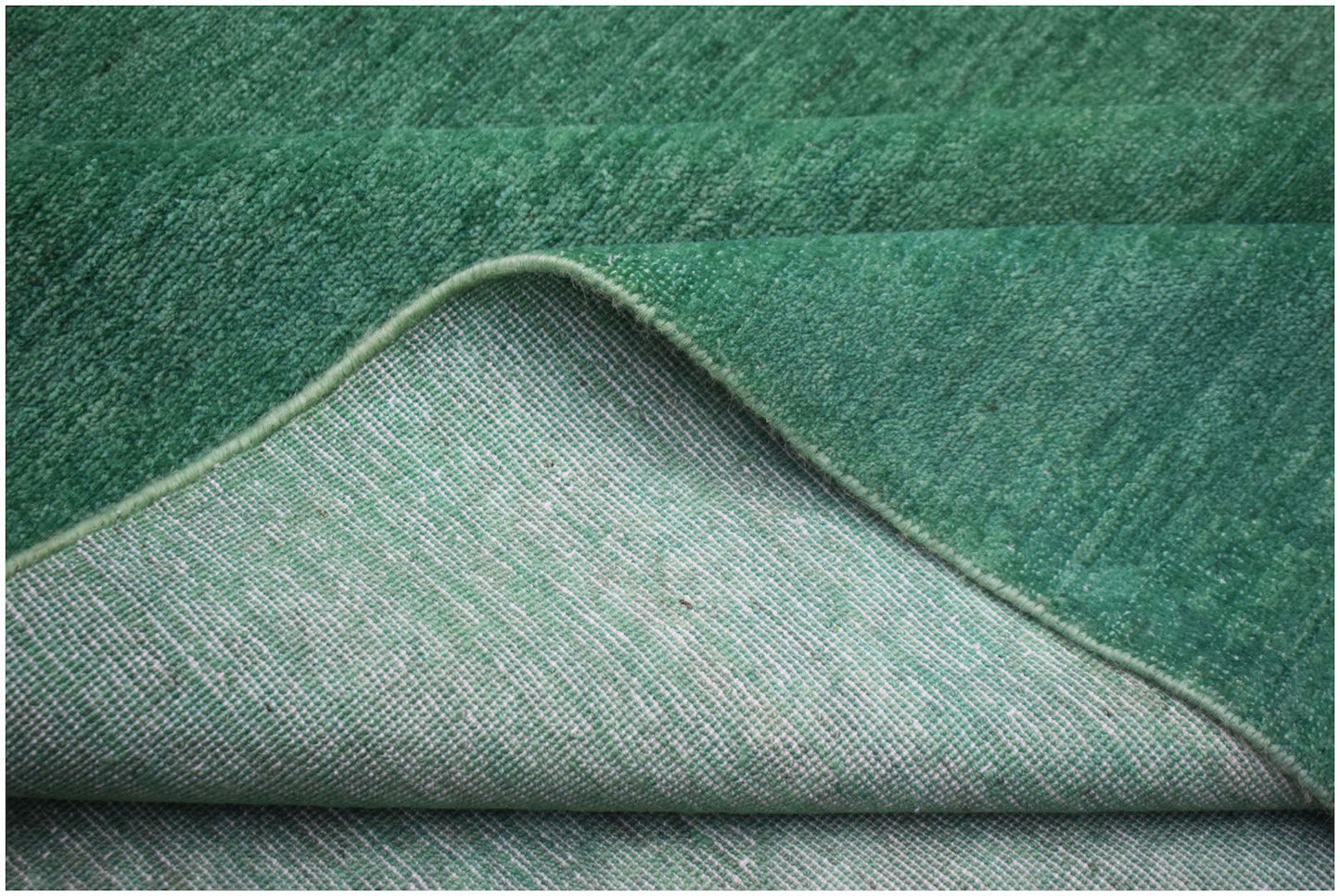 A corner of a handwoven green overdyed Afghan Chobi rug showing its wool pile and cotton backing.