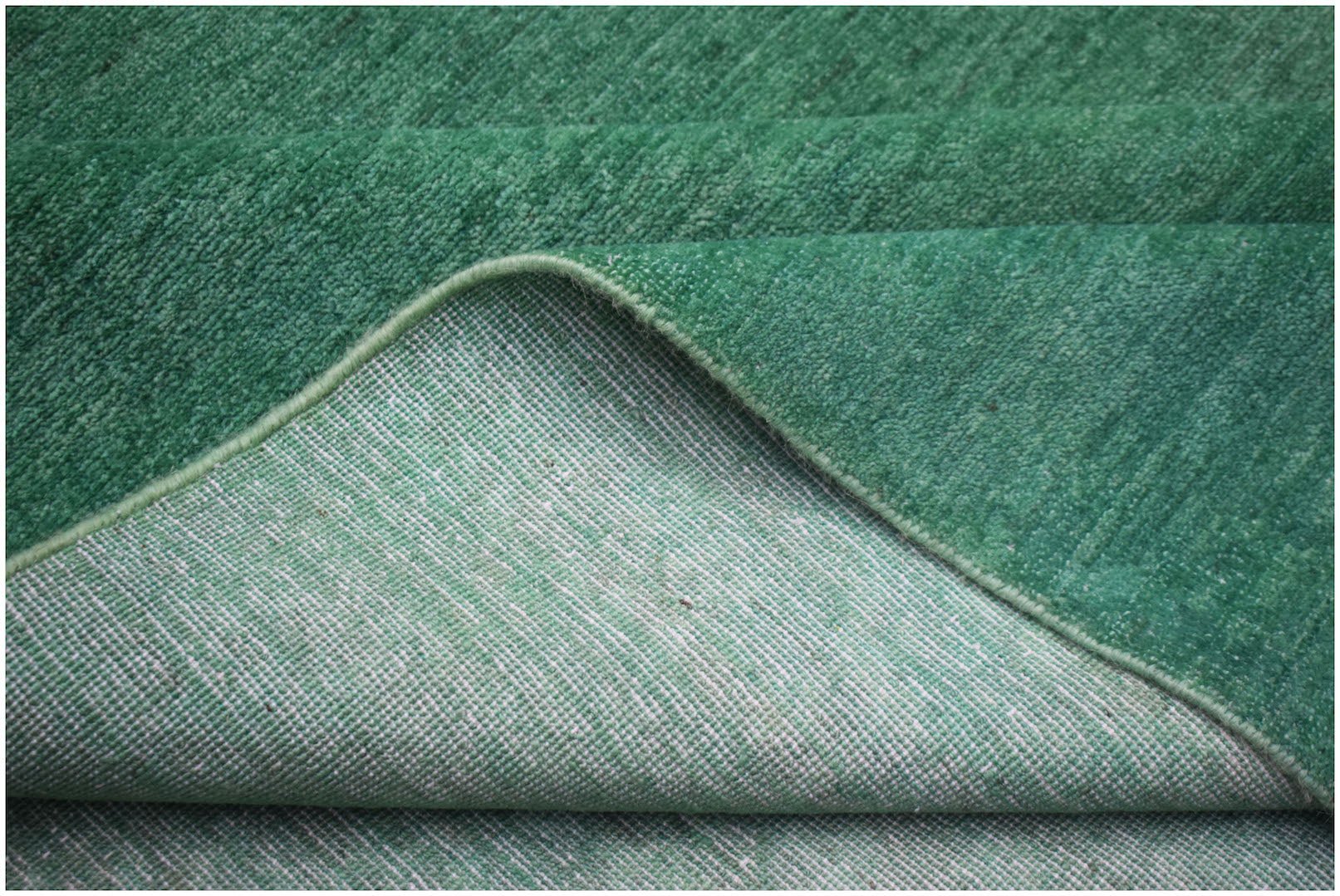 A corner of a handwoven green overdyed Afghan Chobi rug showing its wool pile and cotton backing.