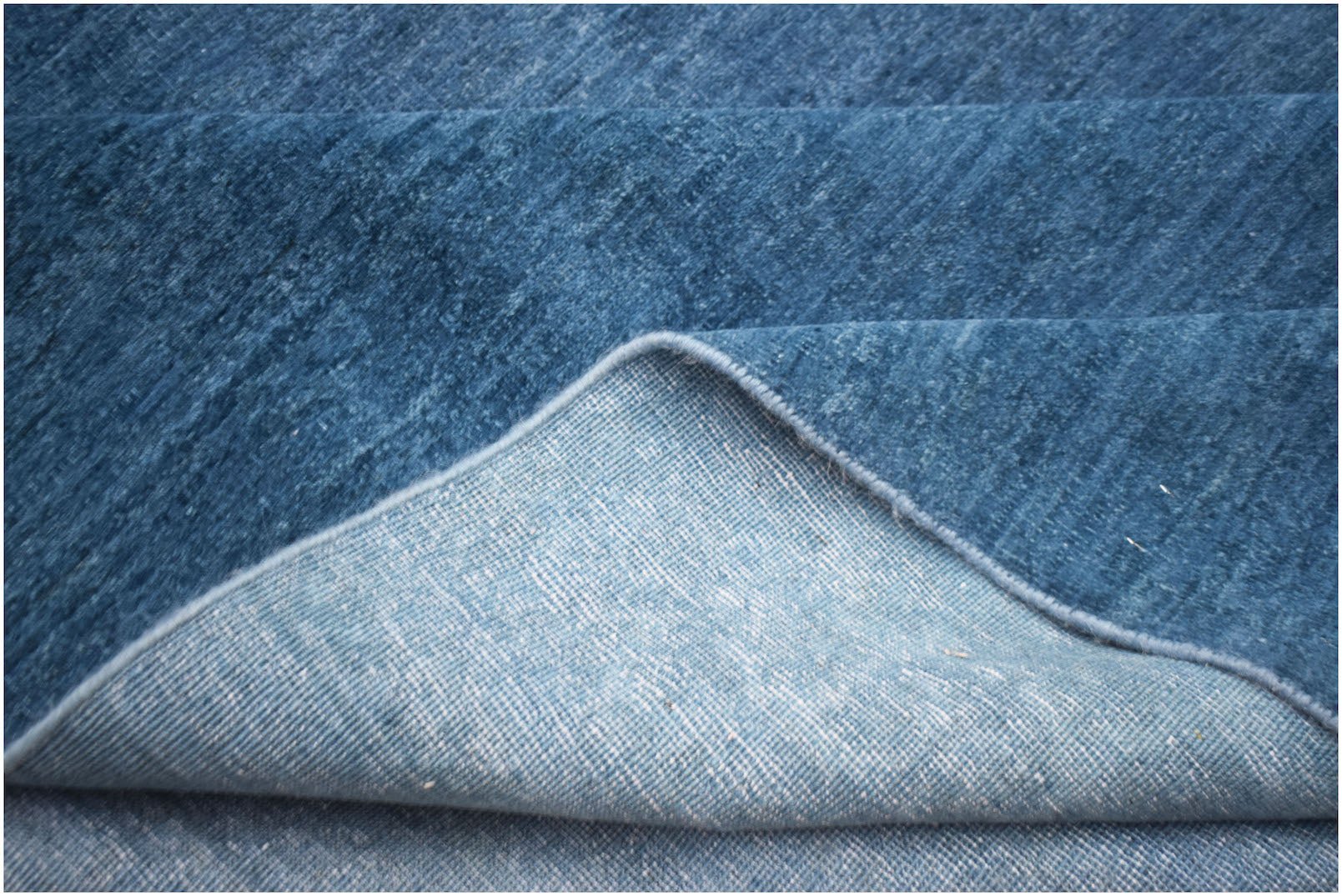 A close-up of a handwoven blue Afghan Chobi rug showing its textured wool pile and cotton backing.