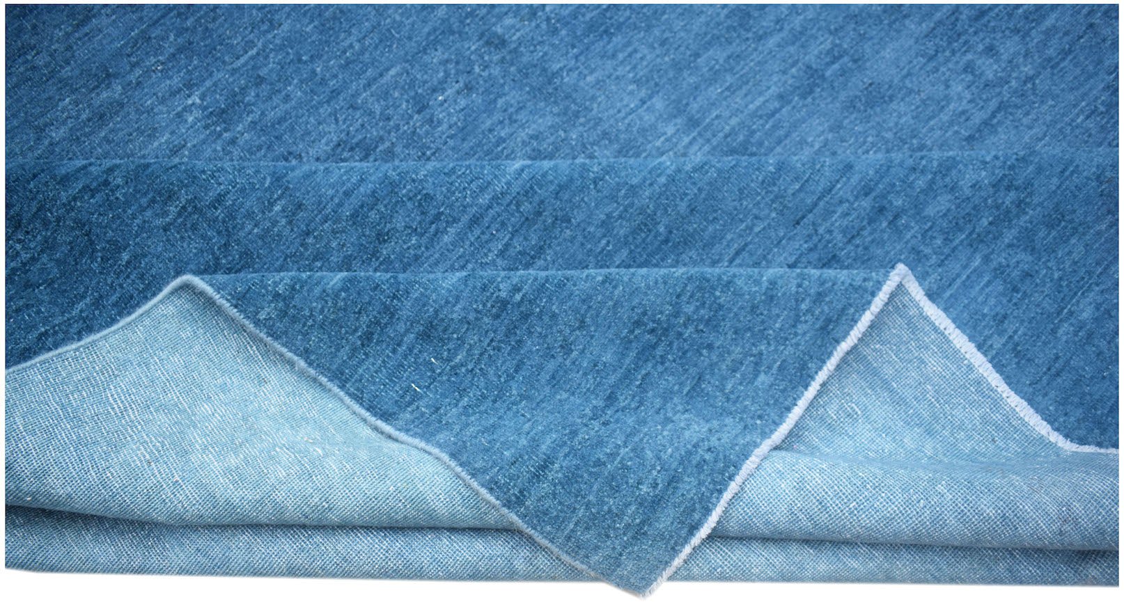 A solid blue handwoven Afghan Chobi rug with a visible cotton foundation on the folded corner.