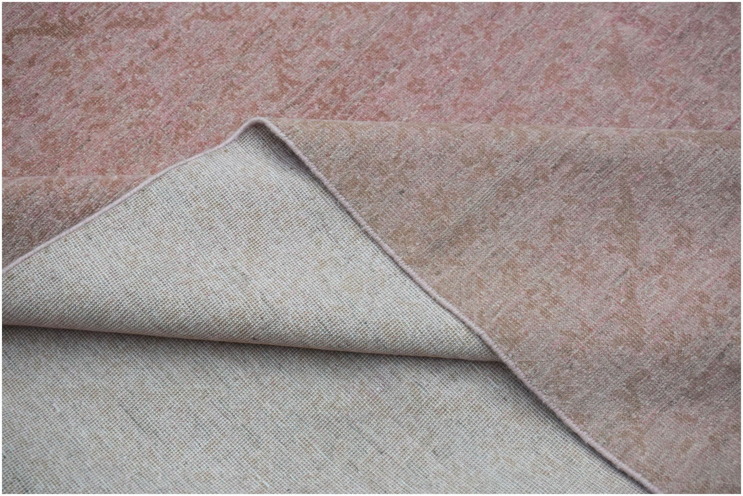 A corner of a handwoven Afghan Chobi rug showing its pink and tan floral pattern and cotton backing.