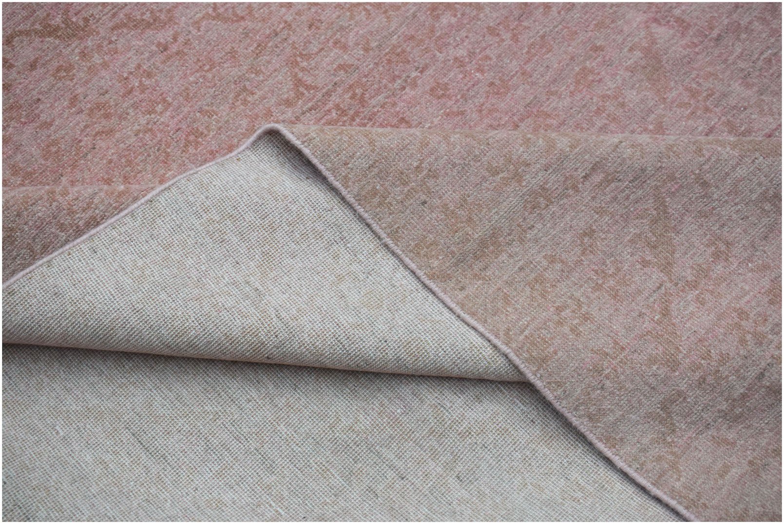 A corner of a handwoven Afghan Chobi rug showing its pink and tan floral pattern and cotton backing.