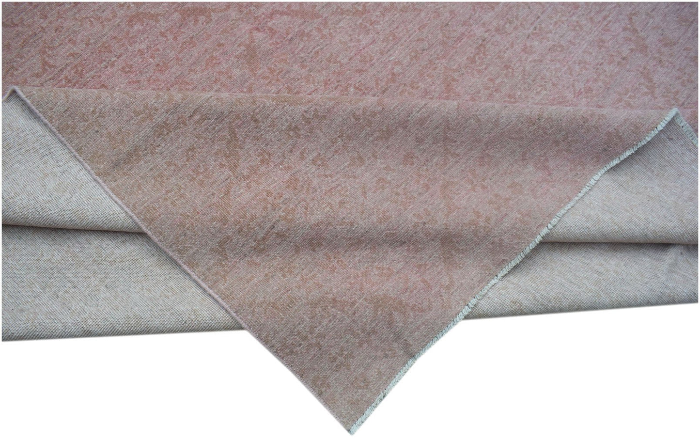 A handmade Afghan Chobi rug in a soft pink tone with a folded corner showing the cotton base.