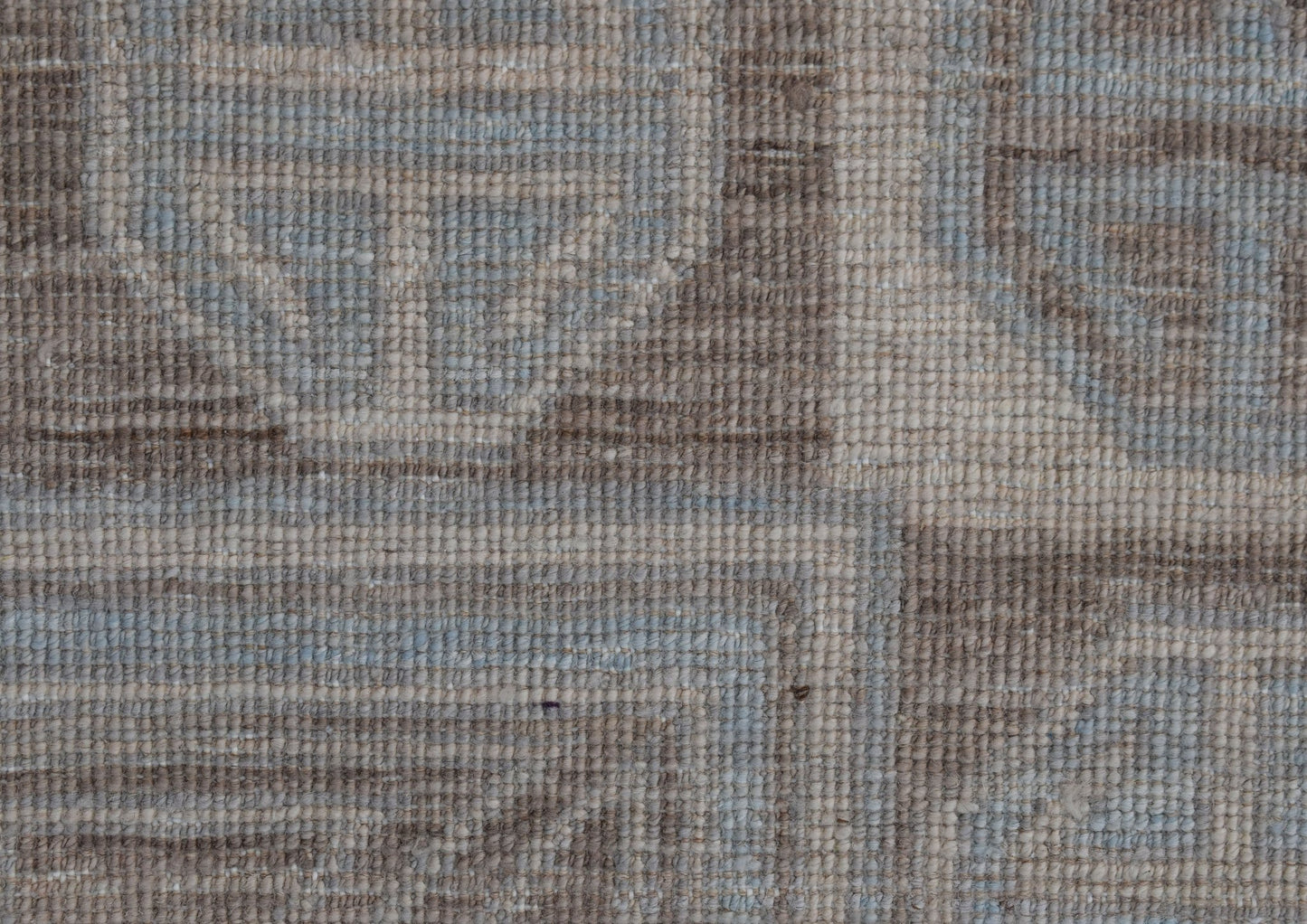 A close-up view of a handwoven wool rug featuring a geometric pattern in soft blue and beige tones.