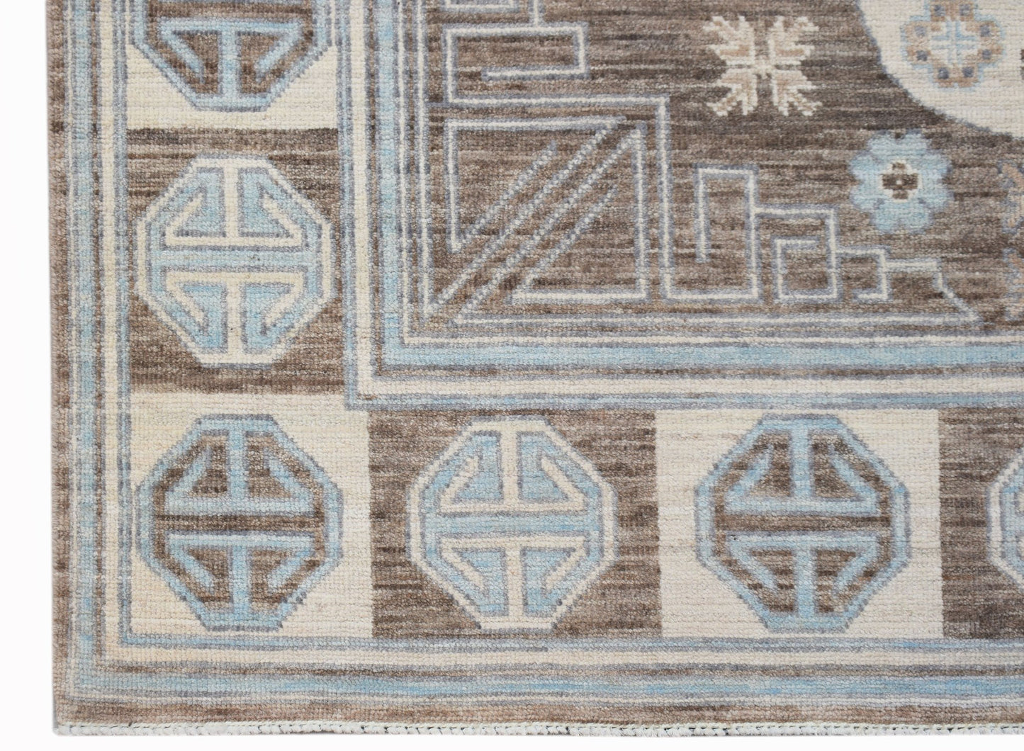 A handmade wool rug featuring a brown and cream geometric border with light blue motifs.