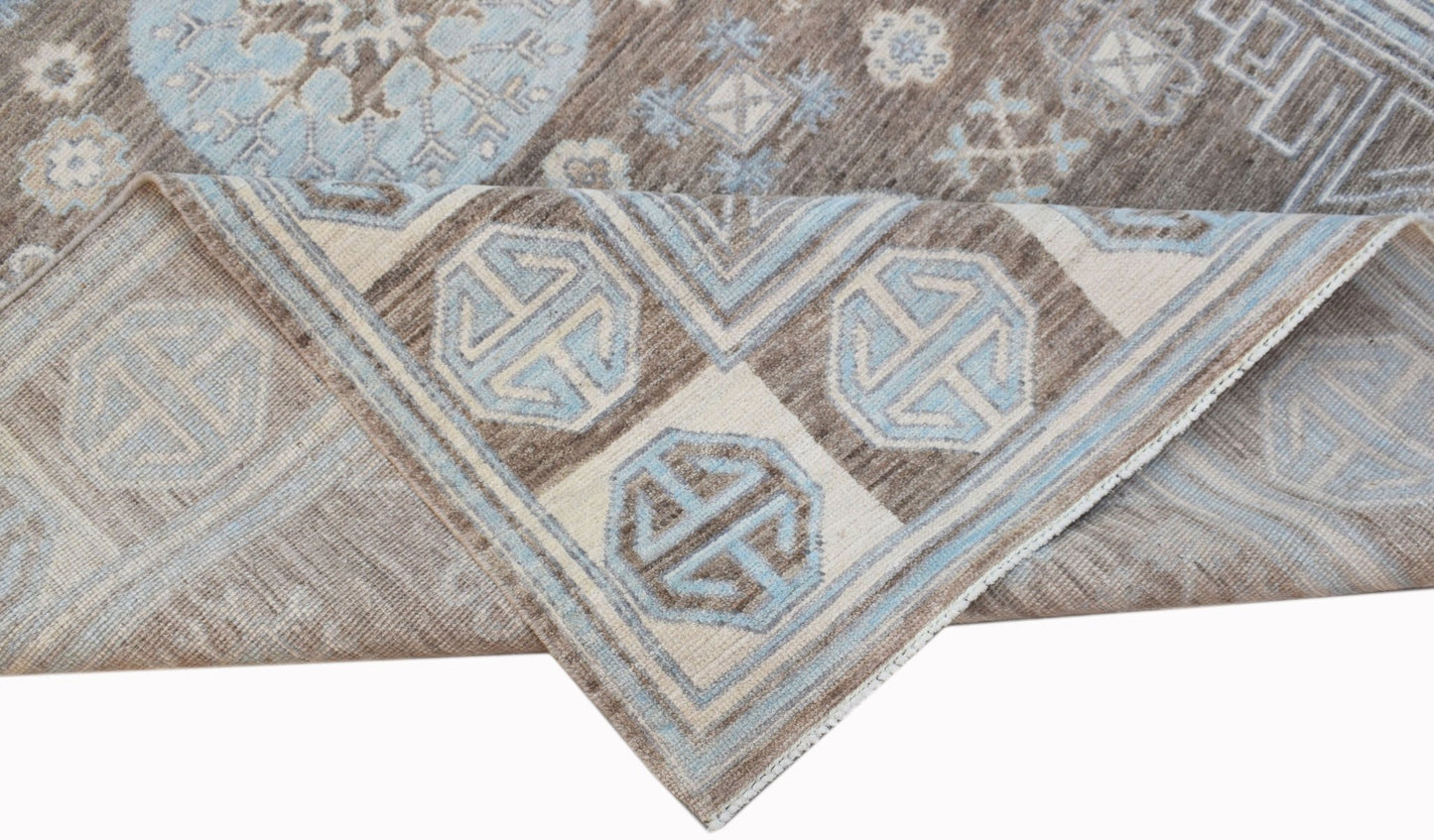 A handmade wool Oushak rug featuring a brown and light blue geometric pattern.