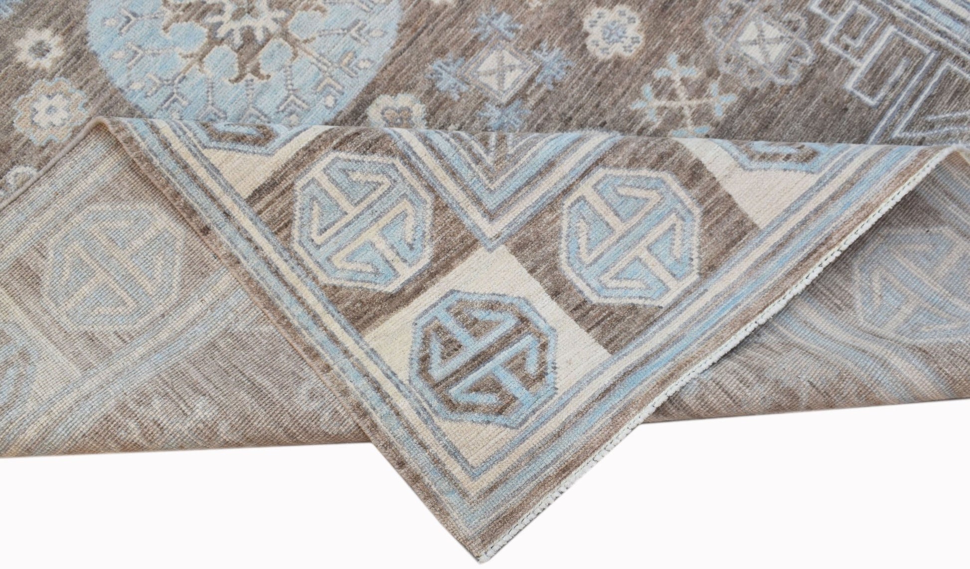 A handmade wool Oushak rug featuring a brown and light blue geometric pattern.