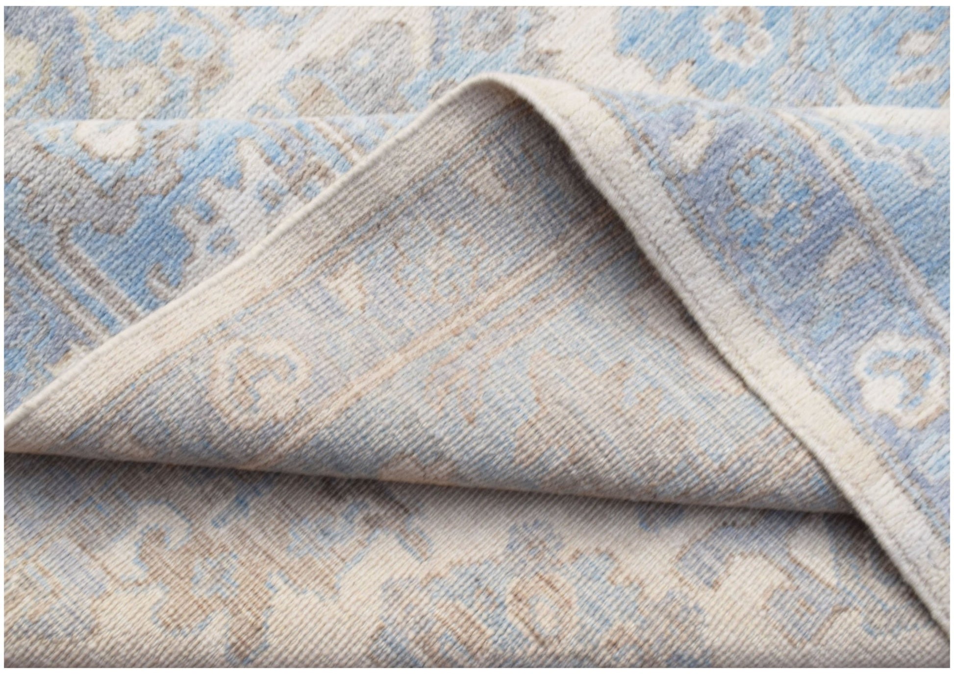 A folded transitional Oushak rug featuring a soft blue and beige traditional pattern.