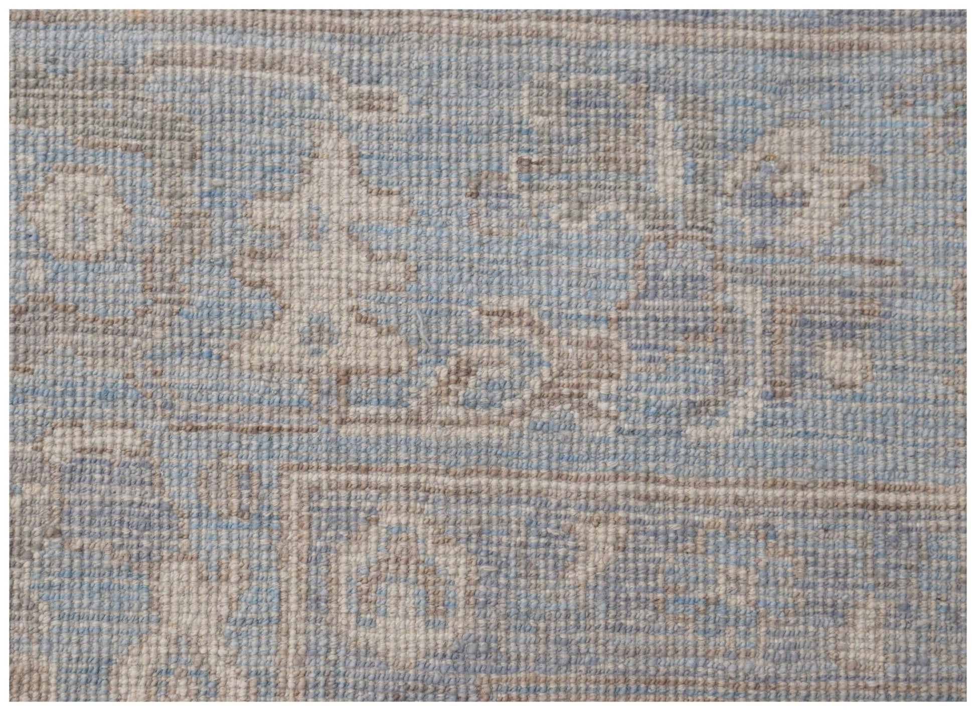 A handmade wool rug featuring a traditional Oushak pattern in soft blue and beige tones.
