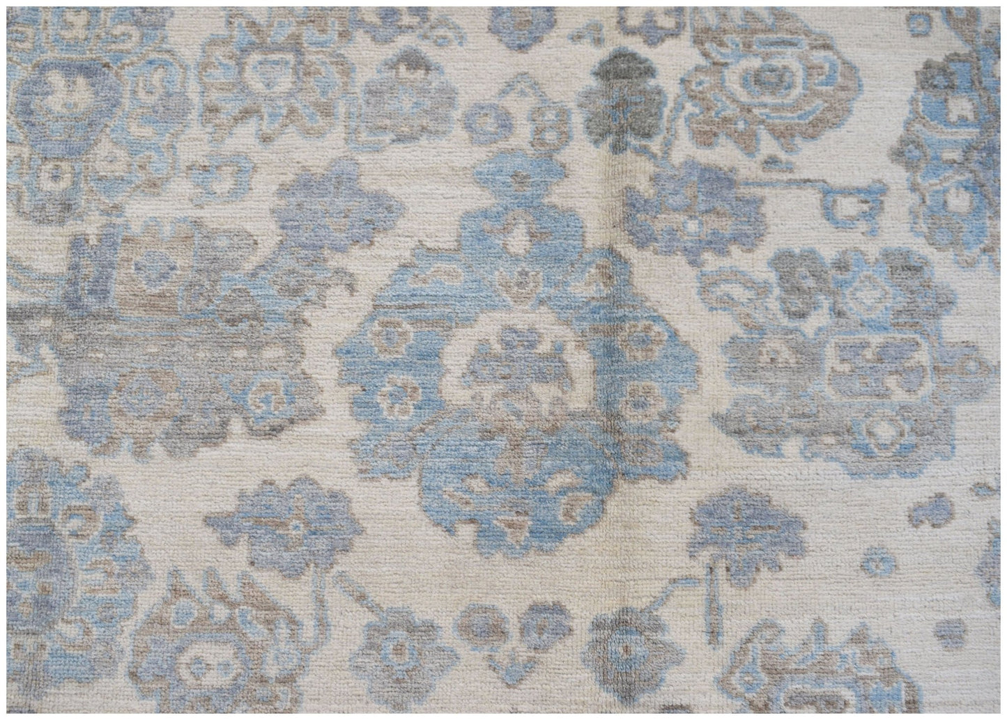 A handmade transitional Oushak rug featuring a soft blue and grey floral pattern on a cream base.
