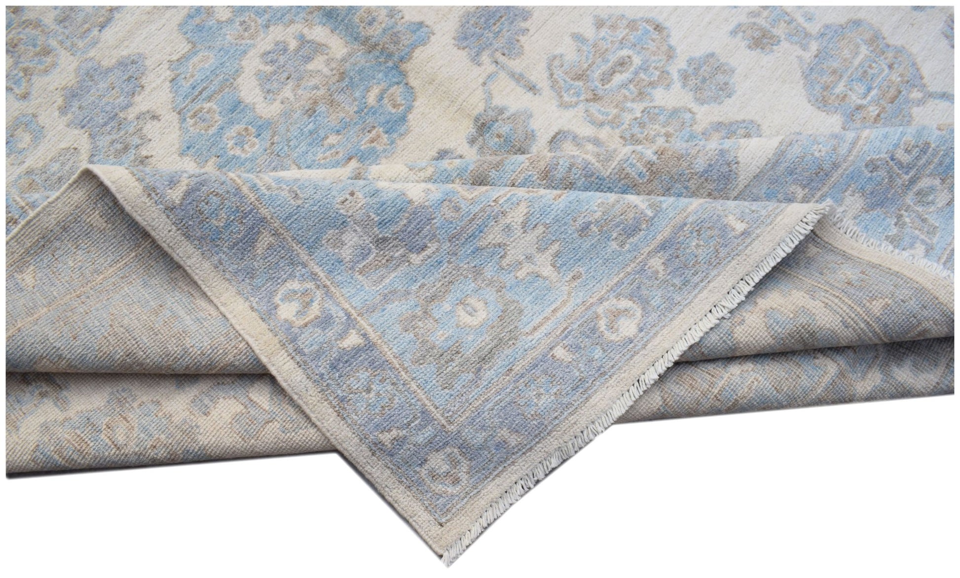 A handmade transitional Oushak rug featuring a blue and beige floral pattern on a wool pile.