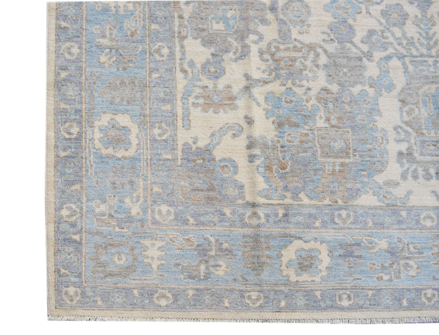 A handmade transitional Oushak rug featuring a blue and beige floral pattern on a wool pile.