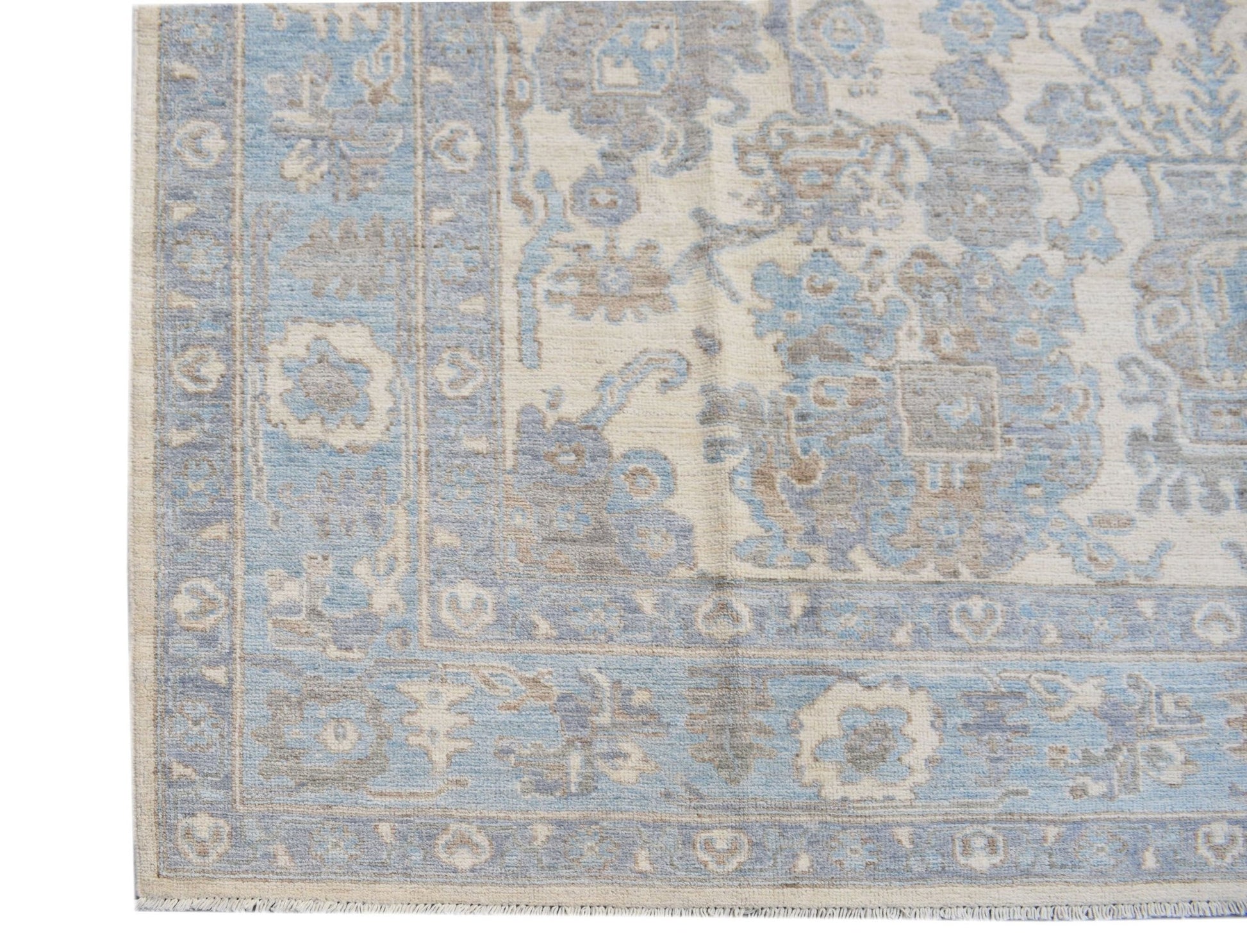 A handmade transitional Oushak rug featuring a blue and beige floral pattern on a wool pile.