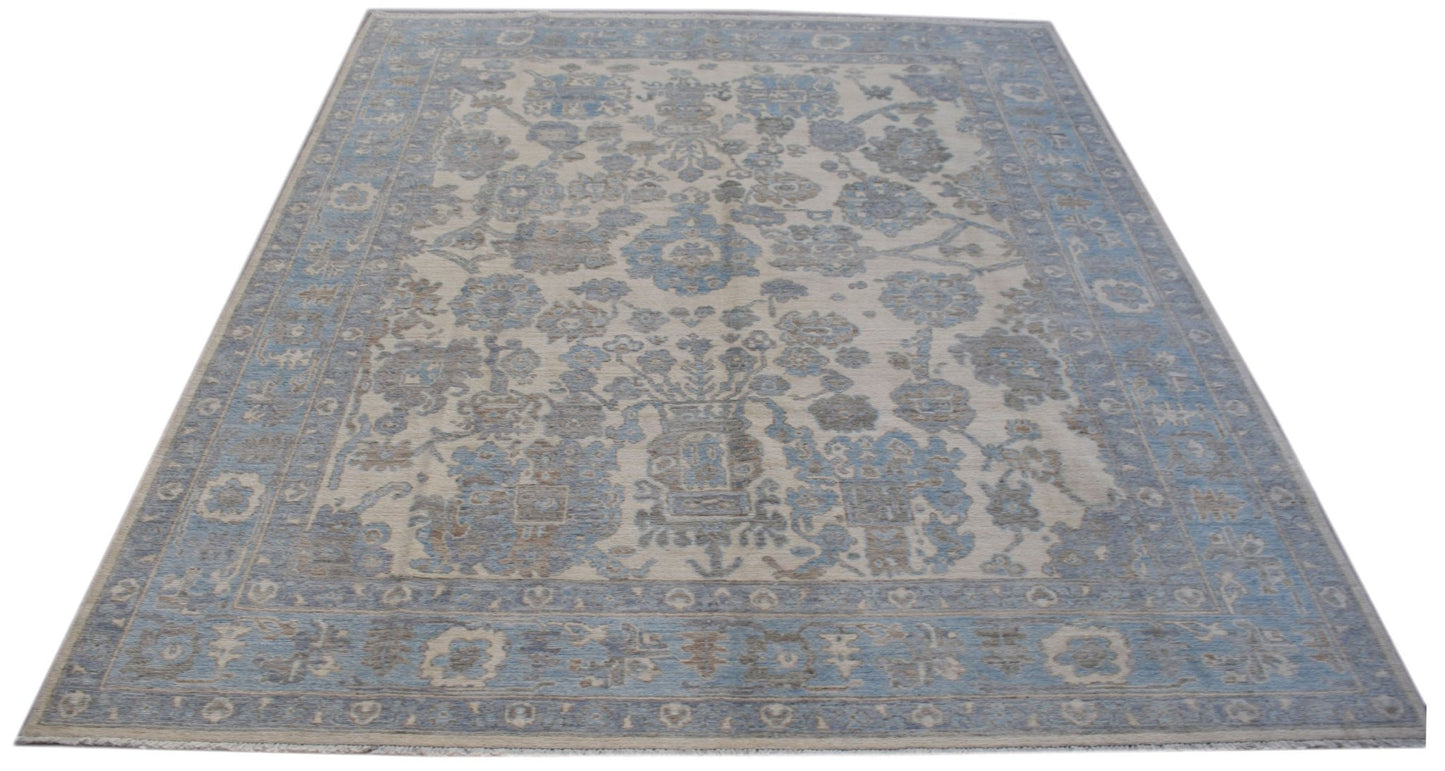 A handmade transitional Oushak rug featuring a blue and beige floral pattern on a wool pile.