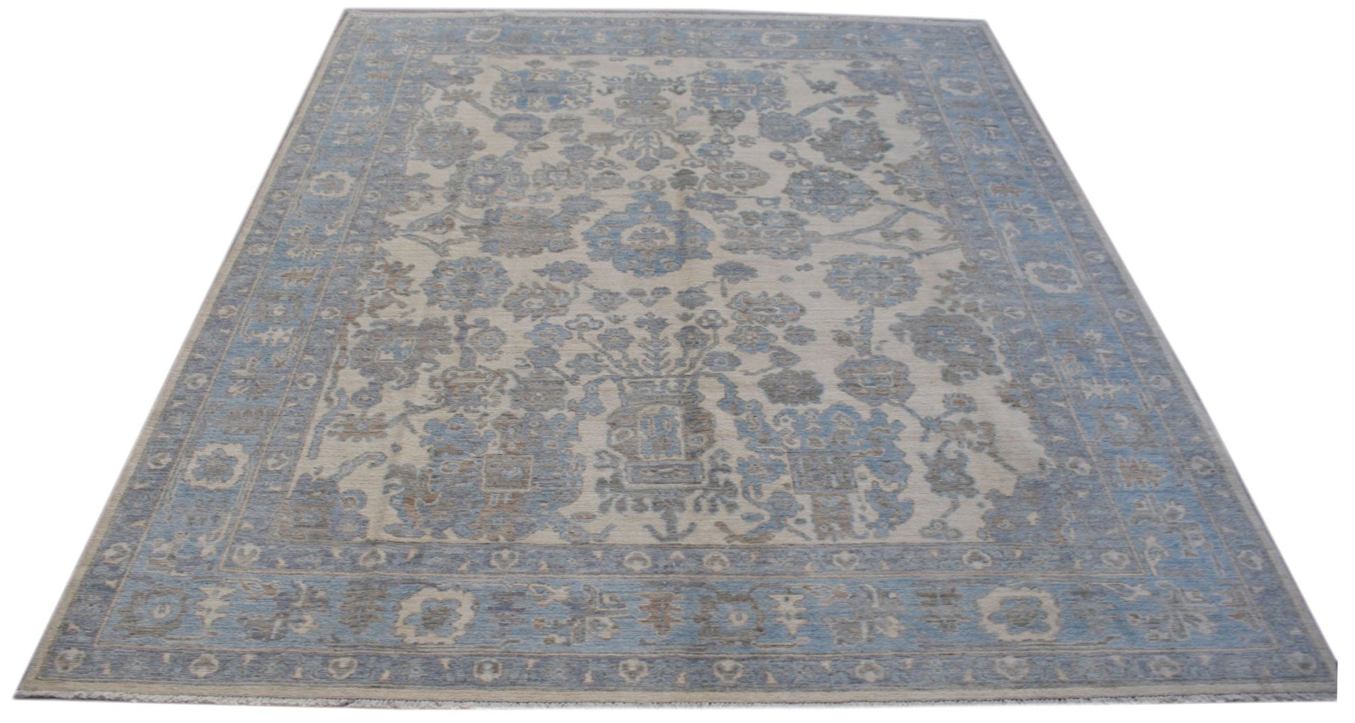 A handmade transitional Oushak rug featuring a blue and beige floral pattern on a wool pile.
