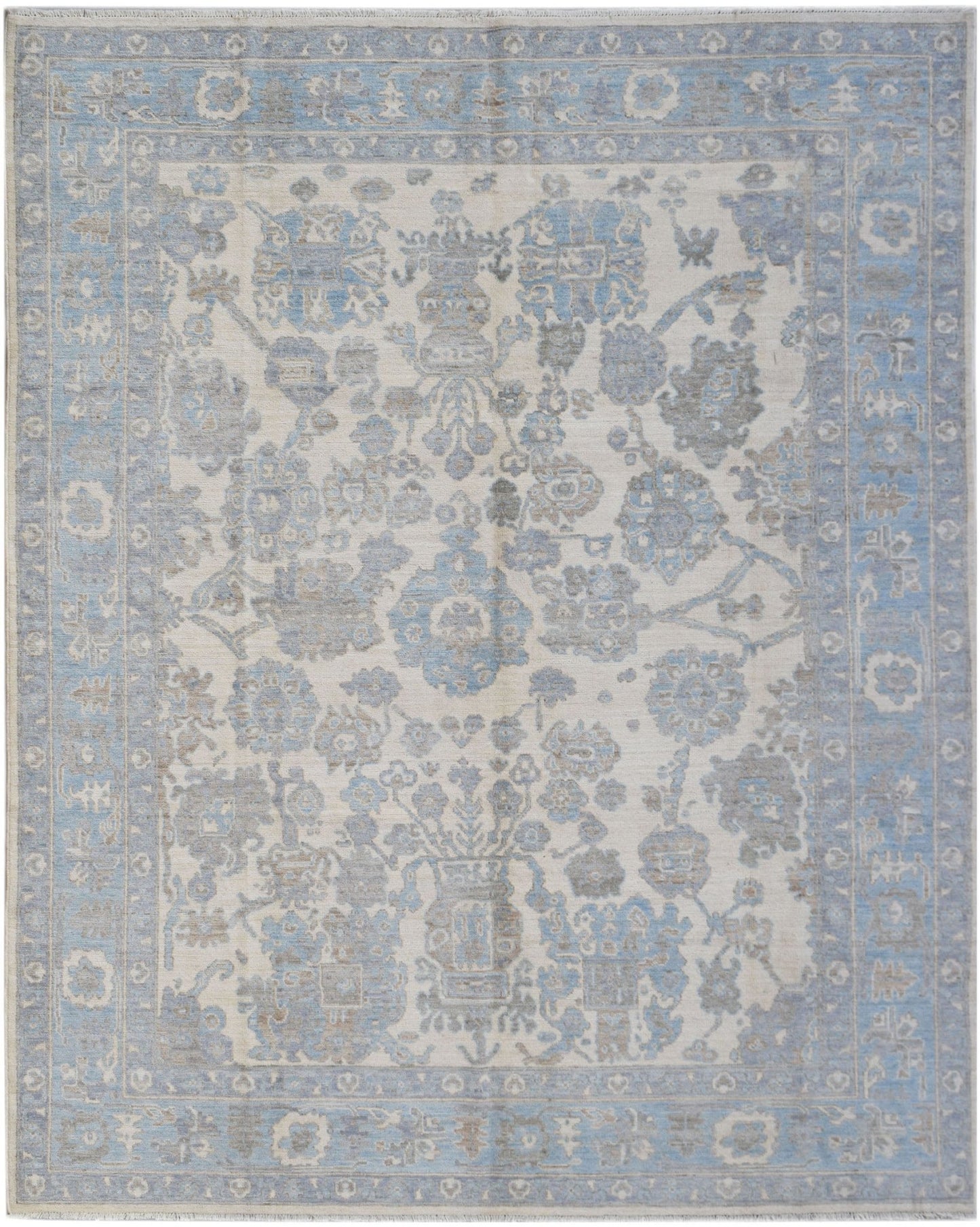 A handmade transitional Oushak rug featuring a soft blue and grey floral pattern on a cream base.