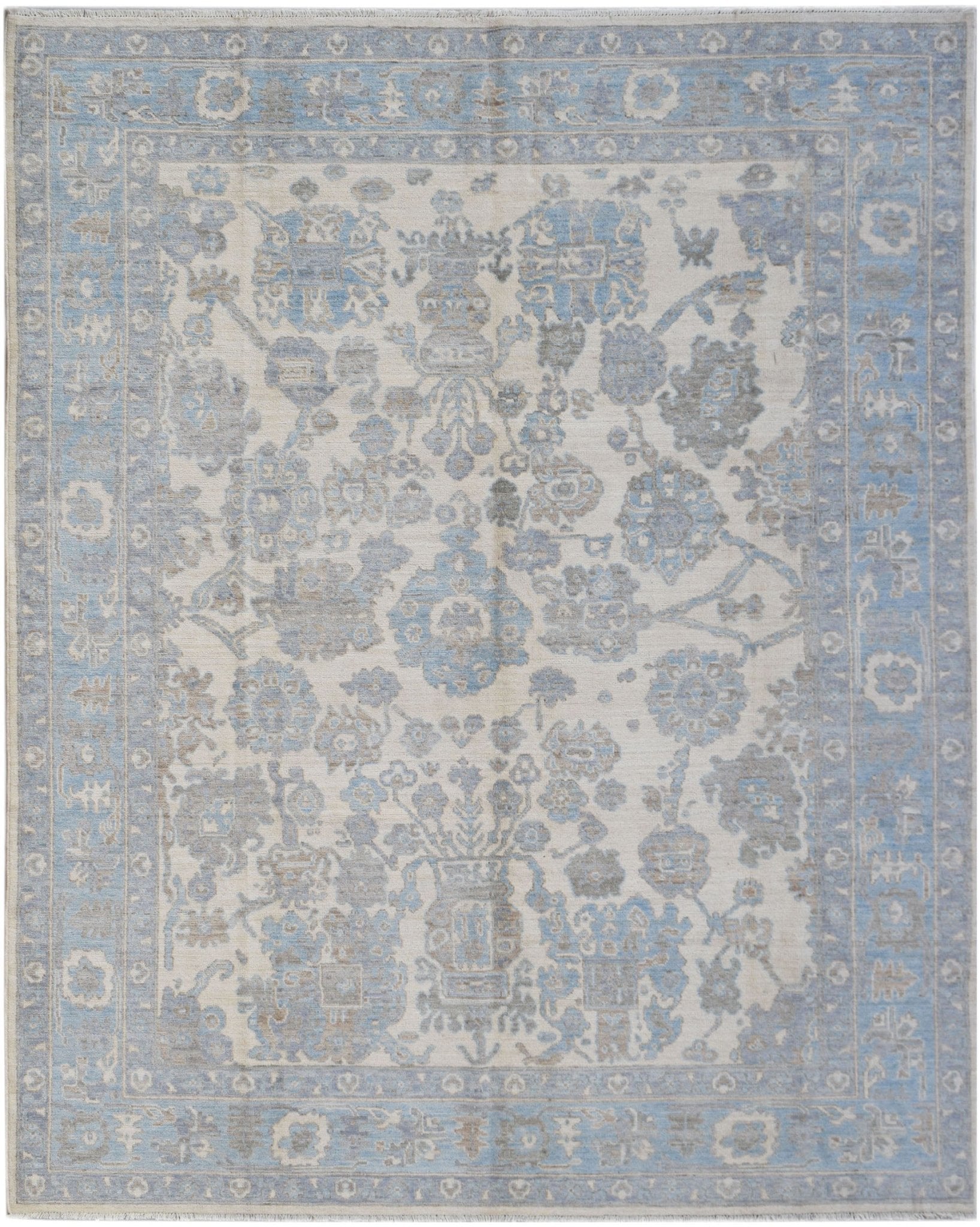 A handmade transitional Oushak rug featuring a soft blue and grey floral pattern on a cream base.