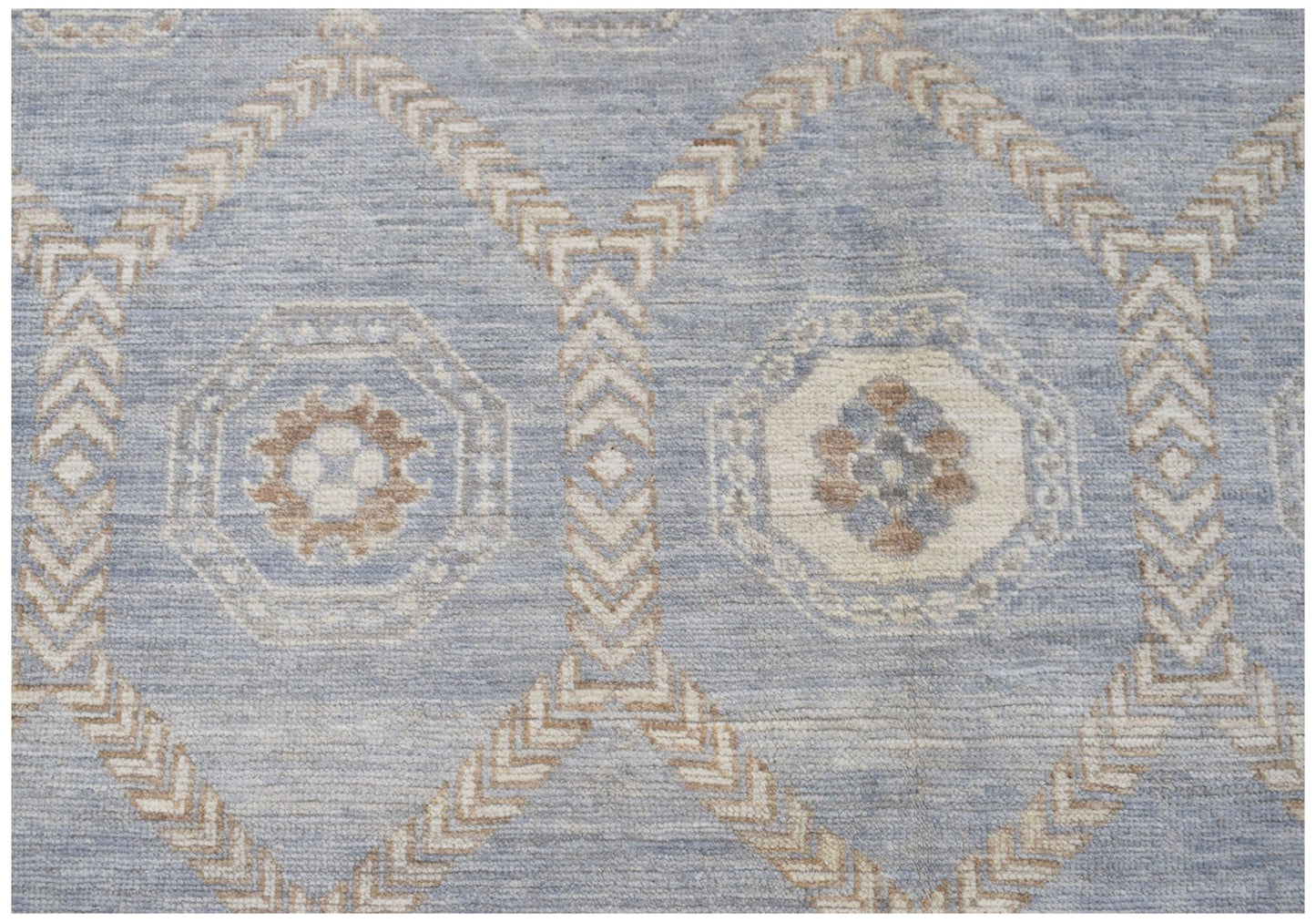 A handmade wool rug featuring a light blue background with a geometric cream and tan pattern.
