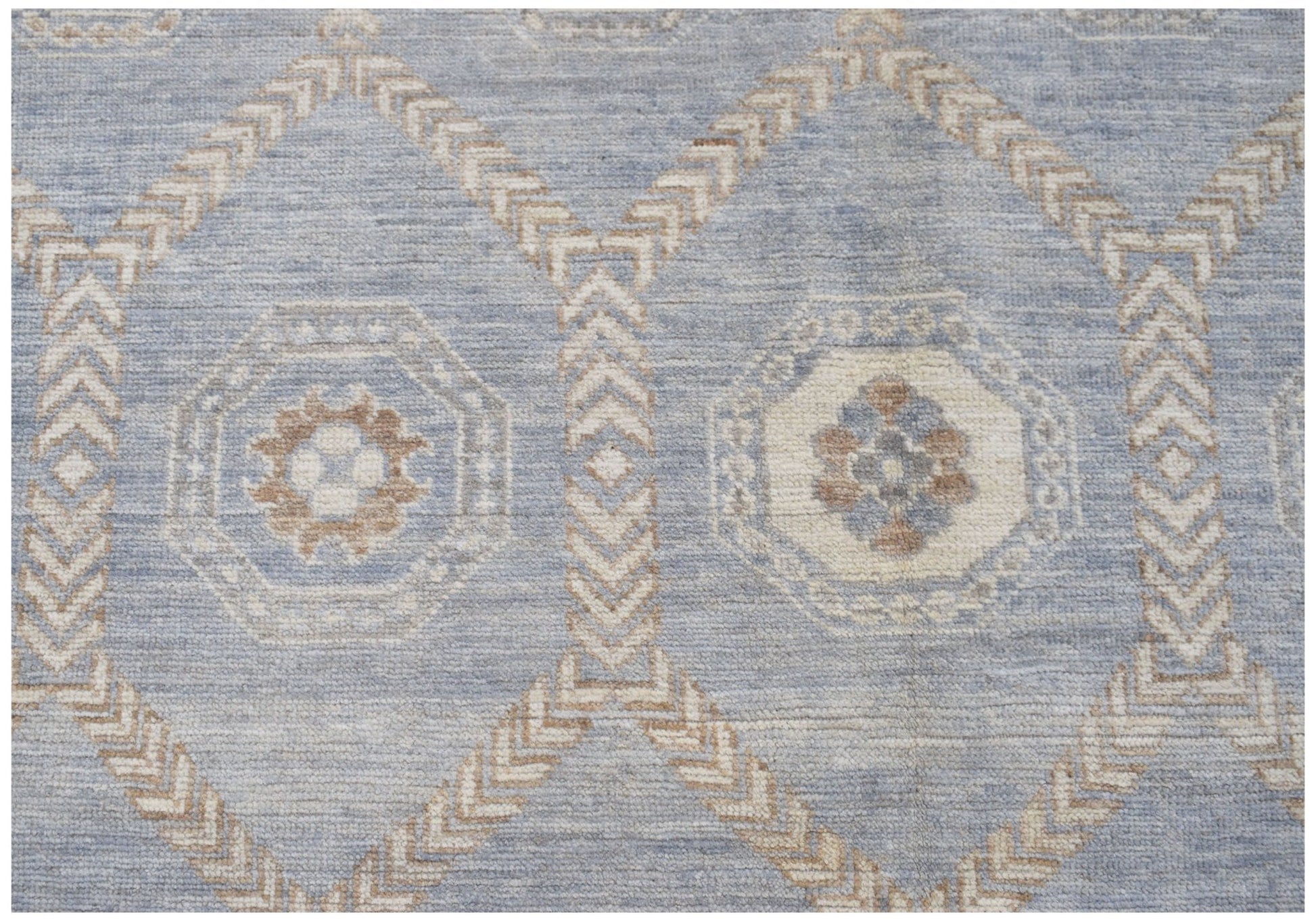 A handmade wool rug featuring a light blue background with a geometric cream and tan pattern.