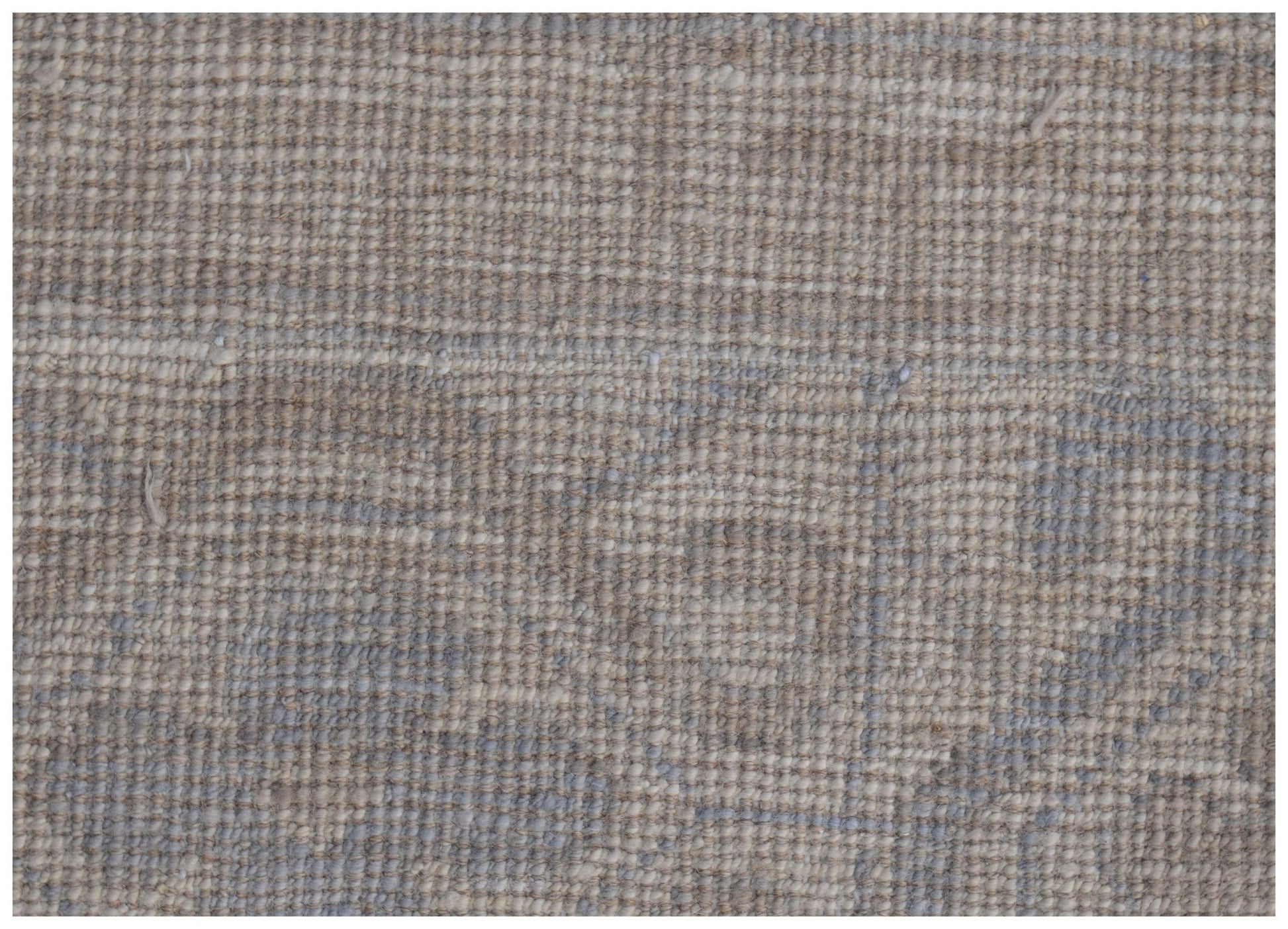A close-up of a handmade wool rug featuring a soft, neutral palette and a subtle, faded pattern.