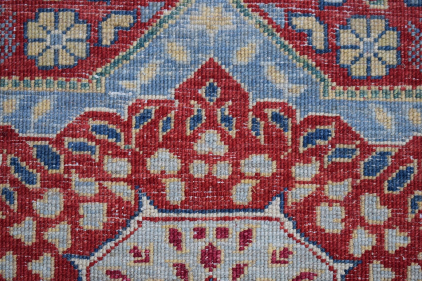 A close-up of a handwoven Afghan Chobi runner featuring a detailed red and blue Mamluk medallion.