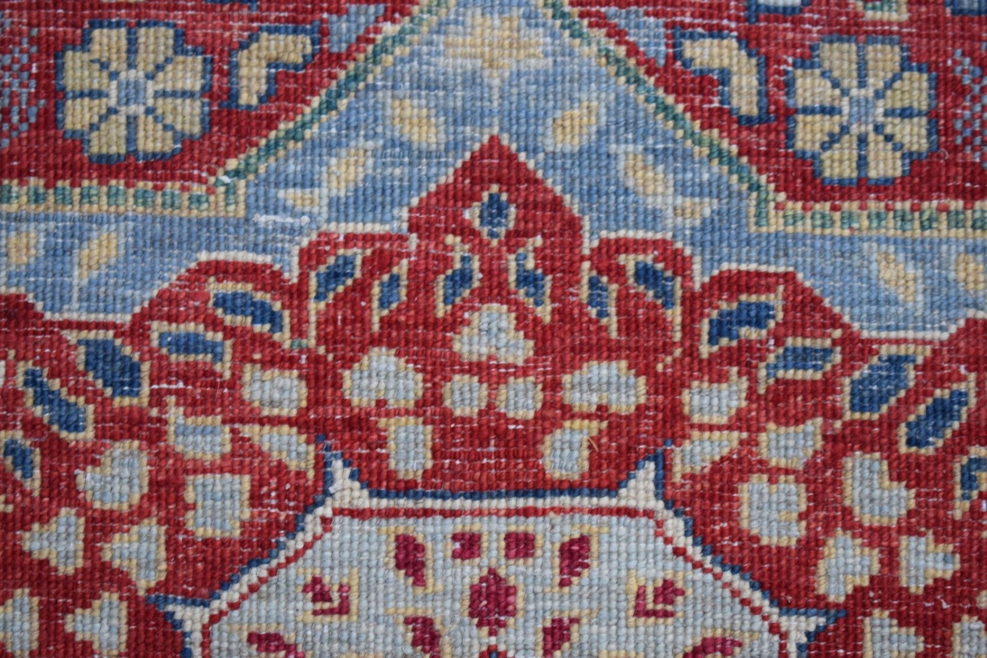 A close-up of a handwoven Afghan Chobi runner featuring a detailed red and blue Mamluk medallion.